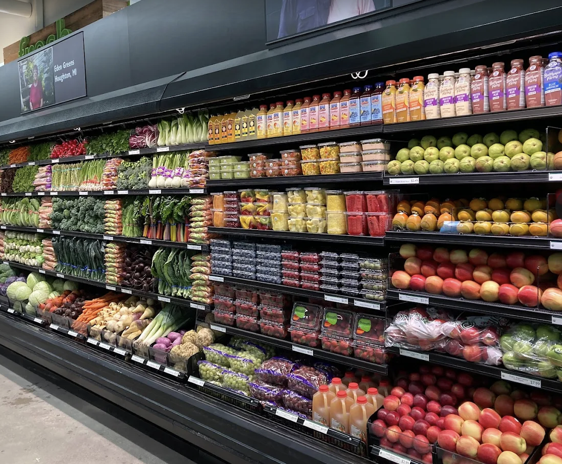 Supermarket produce section with assorted fruits and vegetables, including apples, berries, carrots, radishes, and leafy greens.