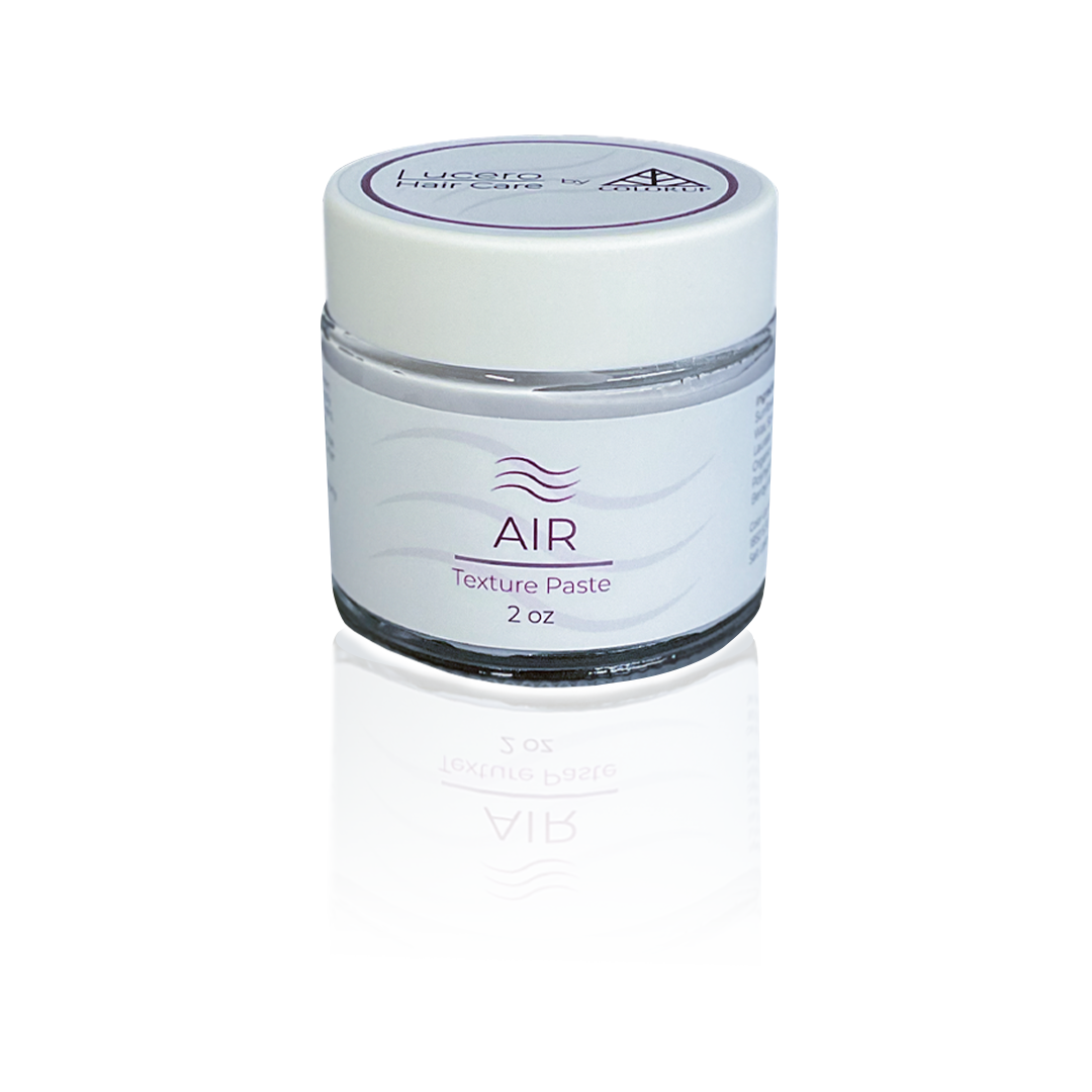 A small white jar labeled 'AIR Texture Paste 2 oz' with a purple logo and text, reflected on a glossy surface, against a light background.