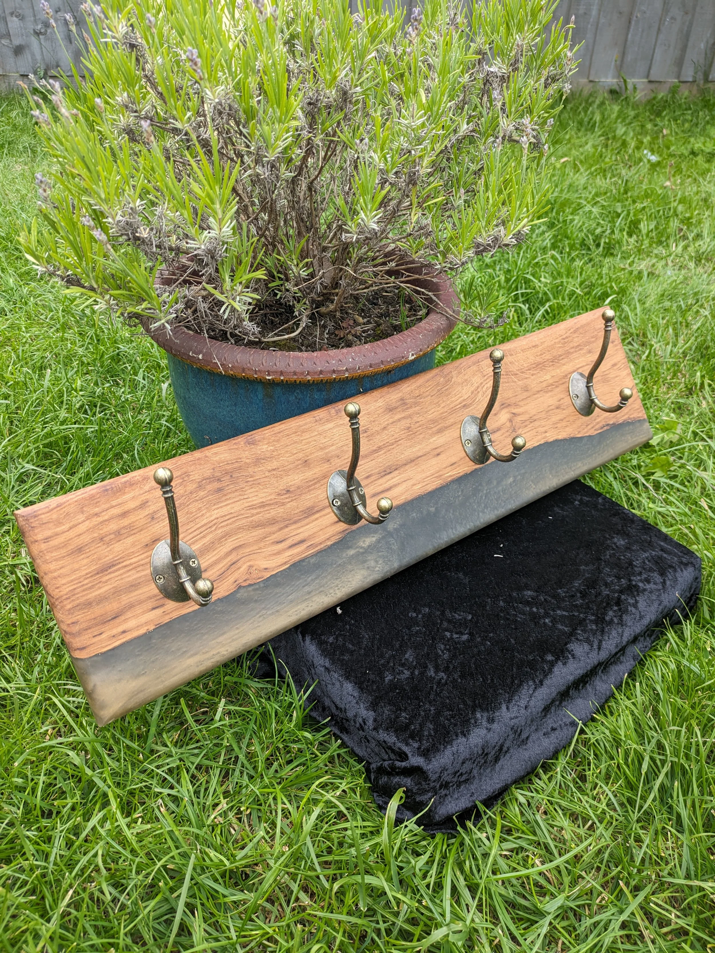 A potted lavender plant sits on a black velvet cloth on the ground, with green grass and a wooden fence in the background.