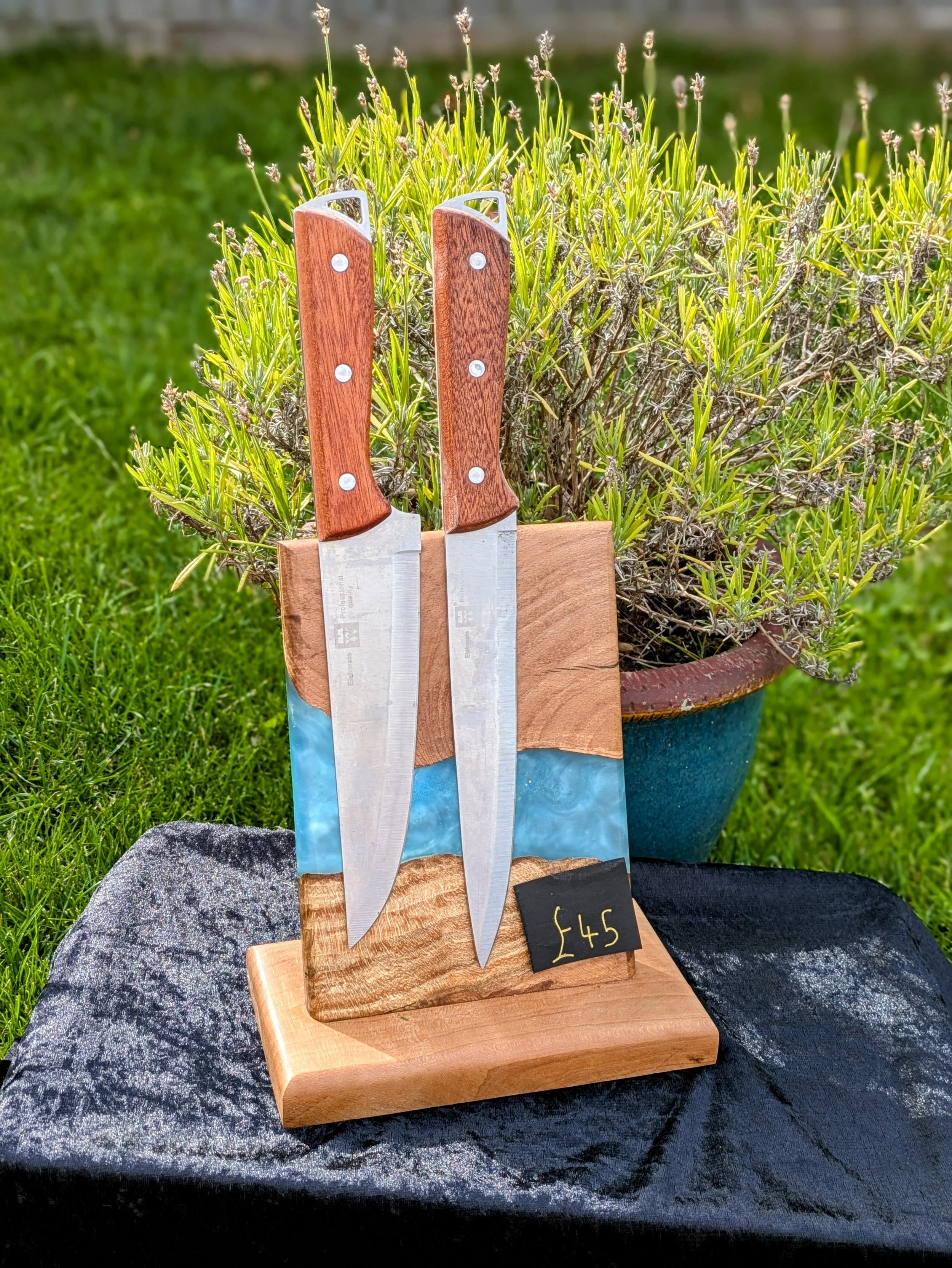 Two kitchen knives with wooden handles in a wooden knife holder, displayed outdoors on a rock with a potted plant in the background, price tag showing £45.