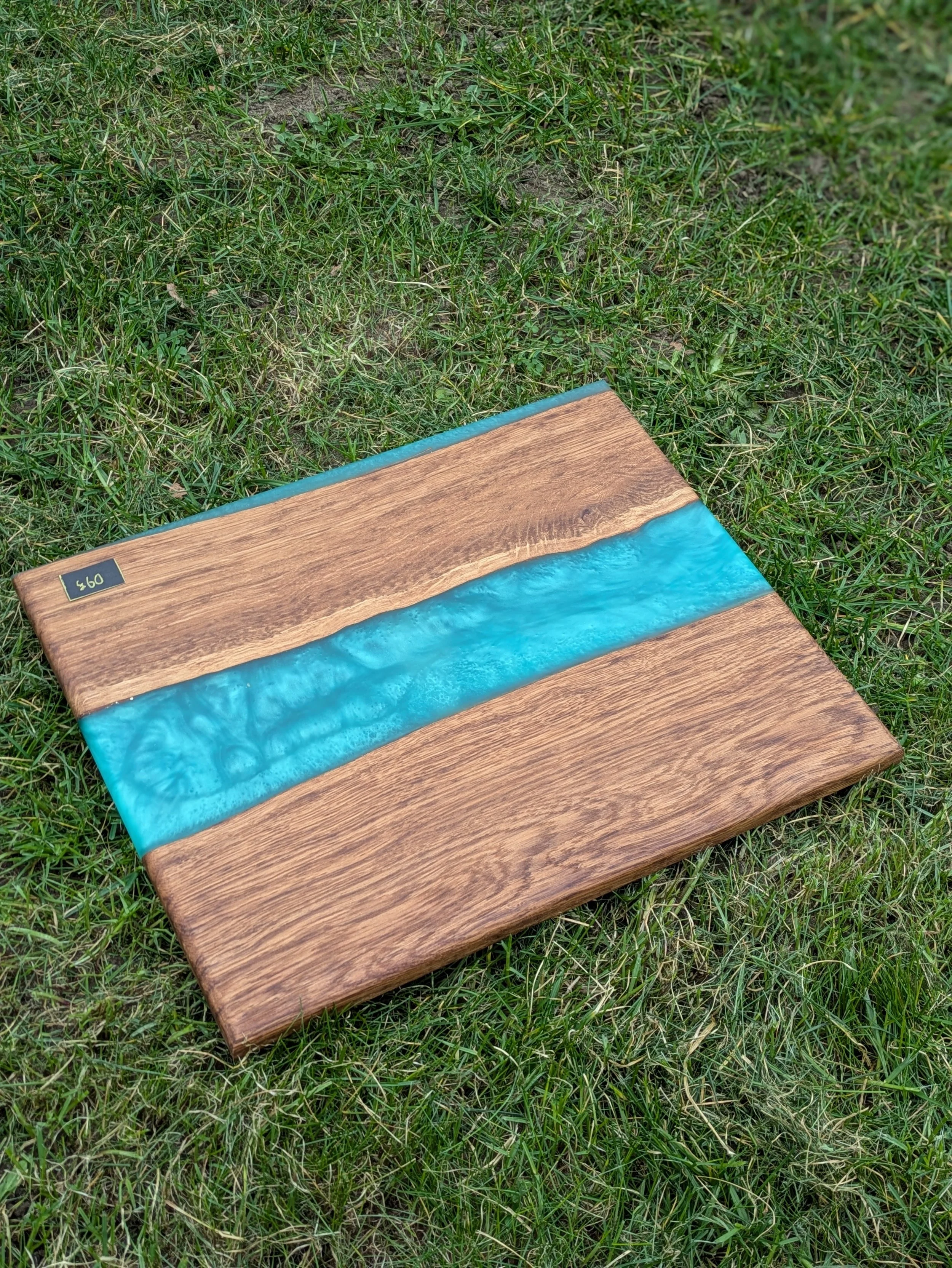Close-up of a wooden table with blue resin accents on a grassy outdoor surface.
