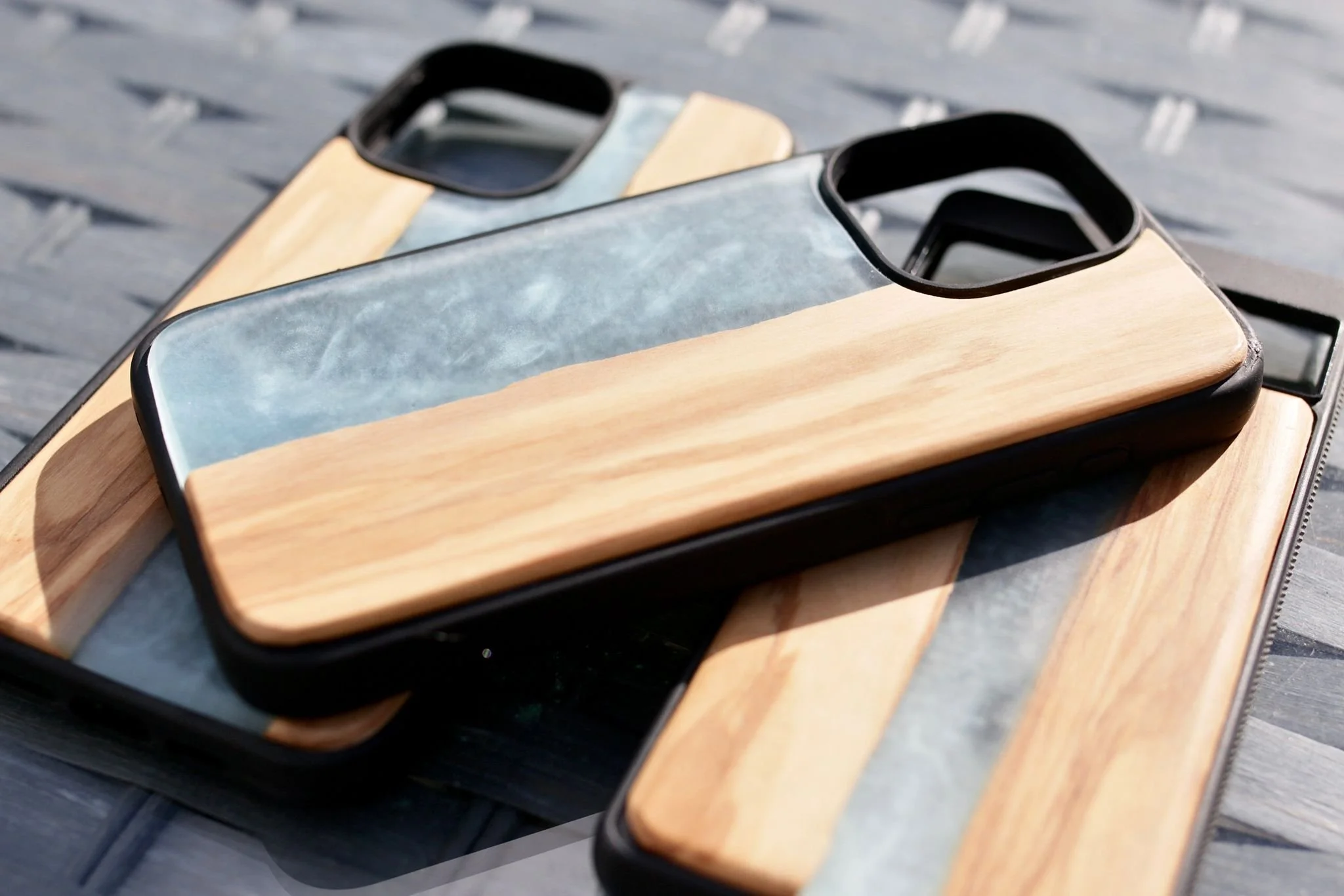 Close-up of two smartphones with wooden and marble backs, placed on a wooden board outdoors.