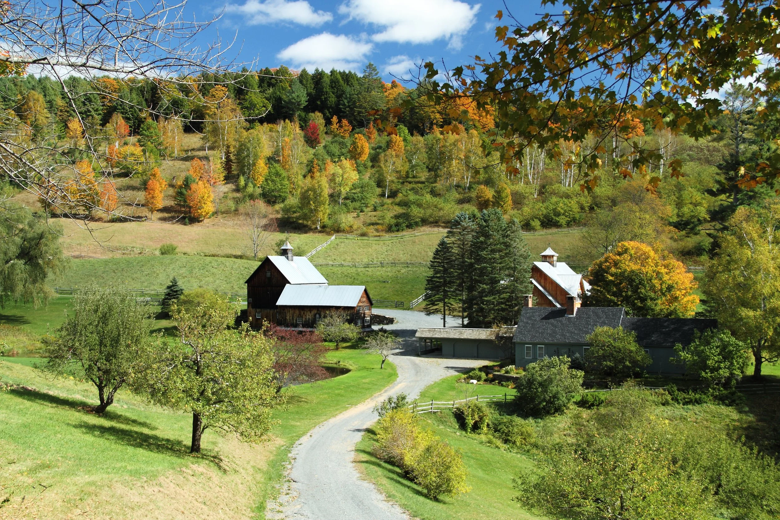 Scenic autumn landscape of a classic New England farm with colorful fall foliage, winding gravel road, rustic barns, and vibrant trees — example of a high-selling stock photography image for travel and landscape photographers.