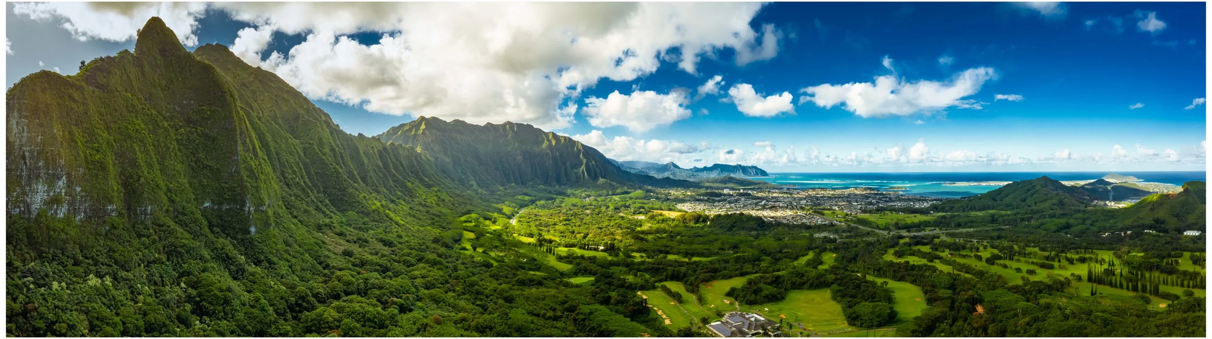 Panoramic aerial view of lush green mountains and coastline on Oahu, Hawaii under bright blue skies — a high-selling tropical landscape stock photo showcasing natural beauty and depth.