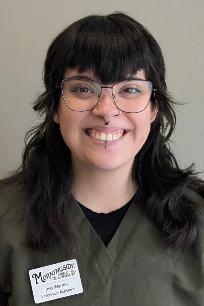 A woman with dark hair, glasses, and a septum piercing smiling, wearing a name tag that says Jess Warren, Veterinary Assistant, at Morningside.