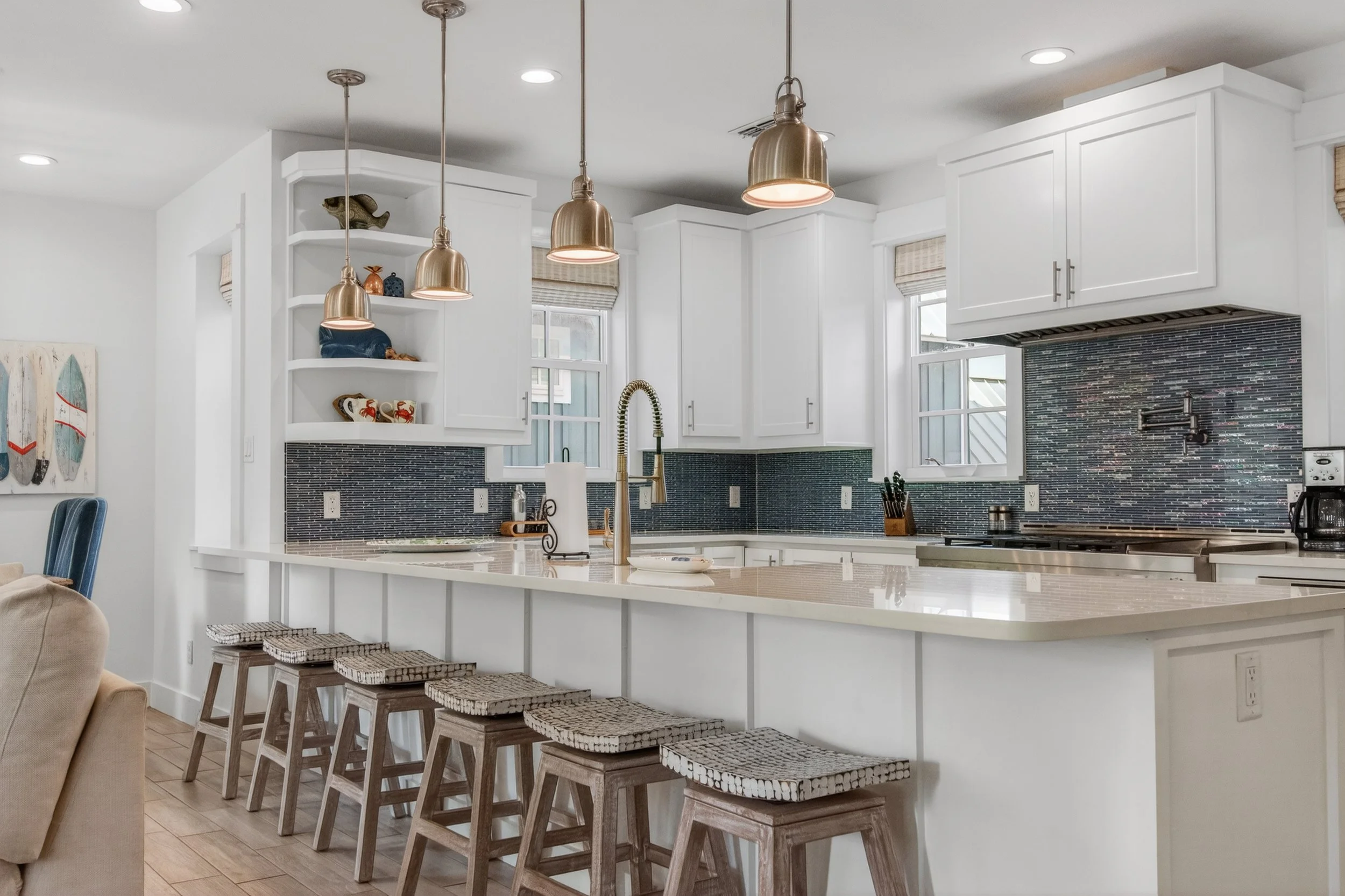 A white kitchen with pendant lighting, white cabinets, a black textured backsplash, and a kitchen island with four woven stools.