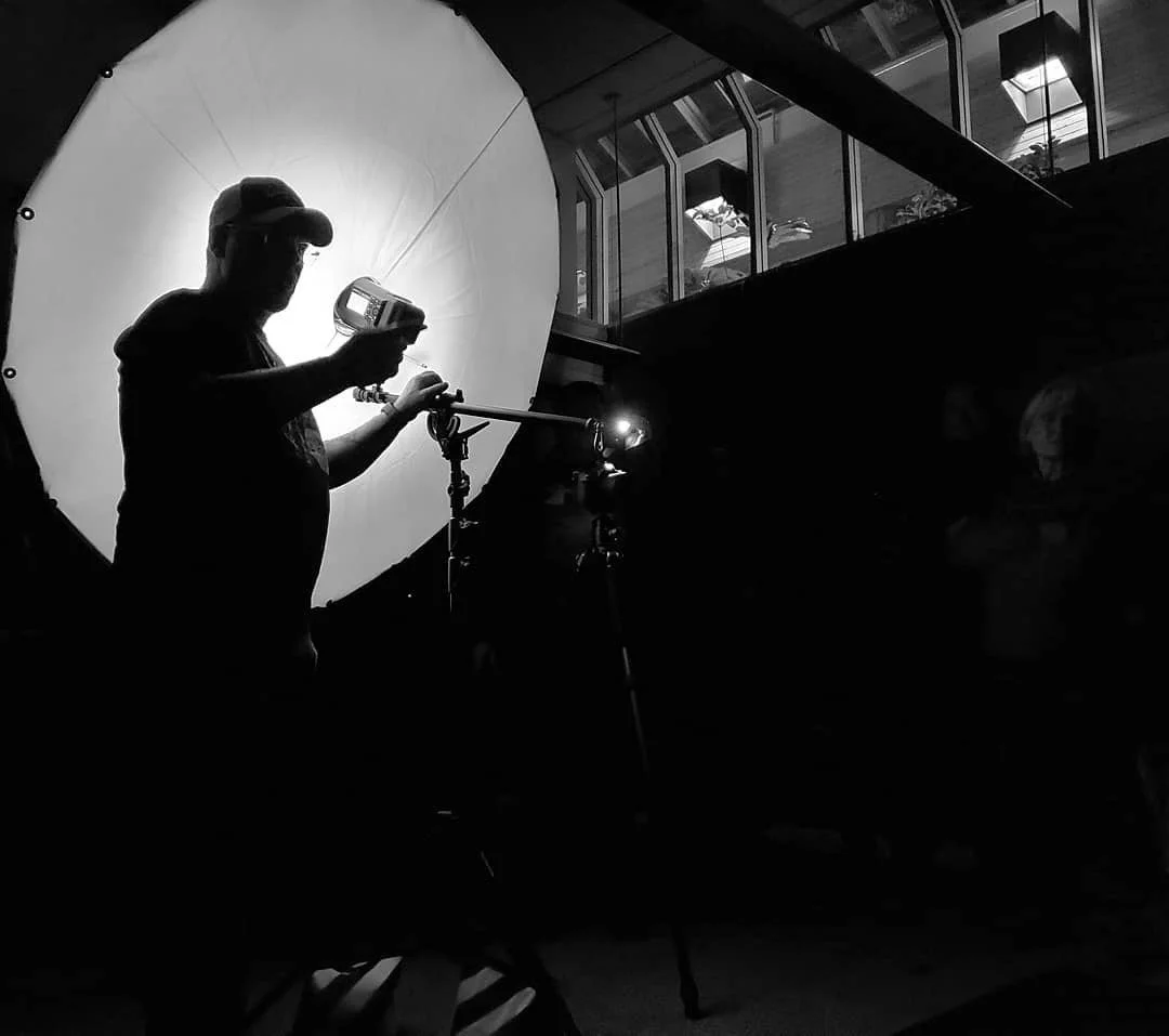 A person using a light meter in front of a large diffuser in a photography studio.