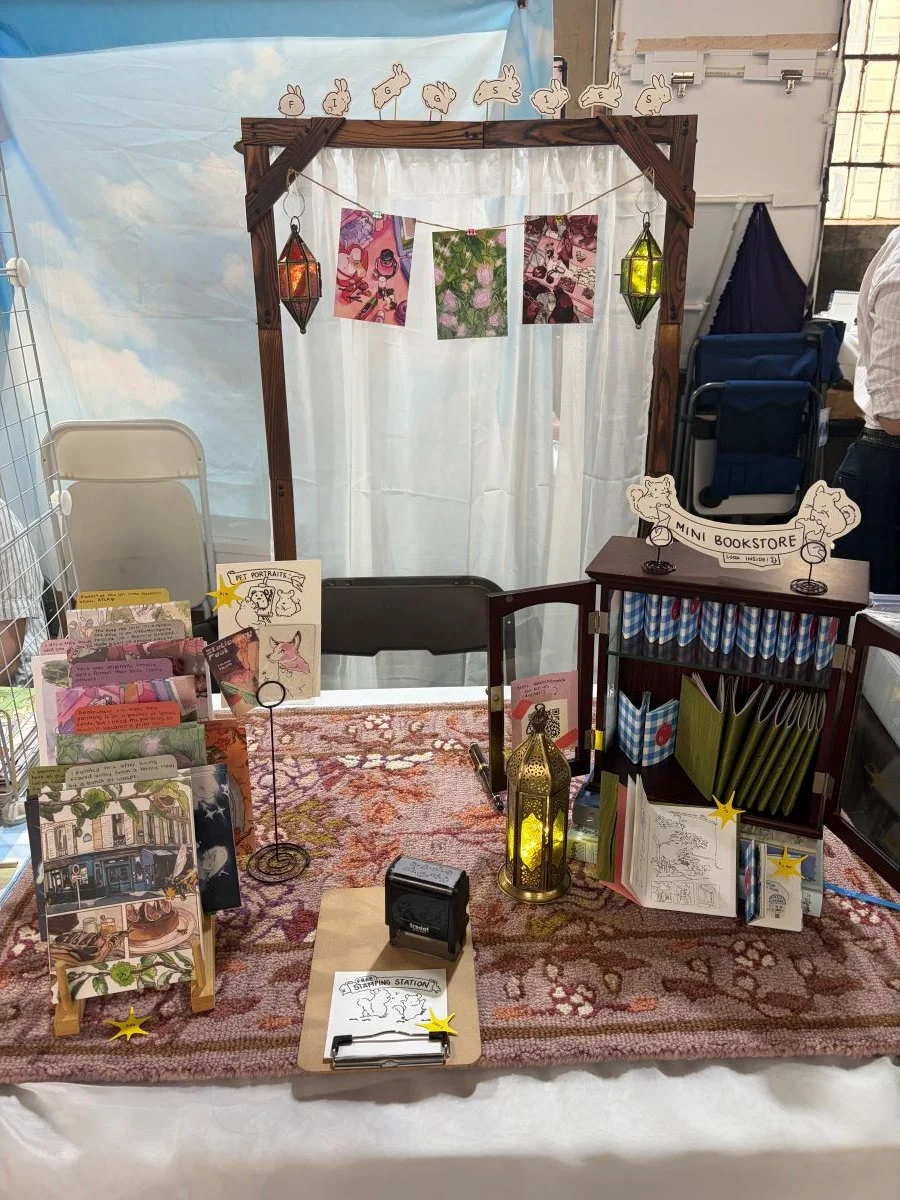 My booth set up kind of looks like the inside of my apartment. I wanted it to feel warm, homey, and magical, complete with a little rug exactly the size of my booth size and mini lanterns.

I left the center open so that people could watch me draw my