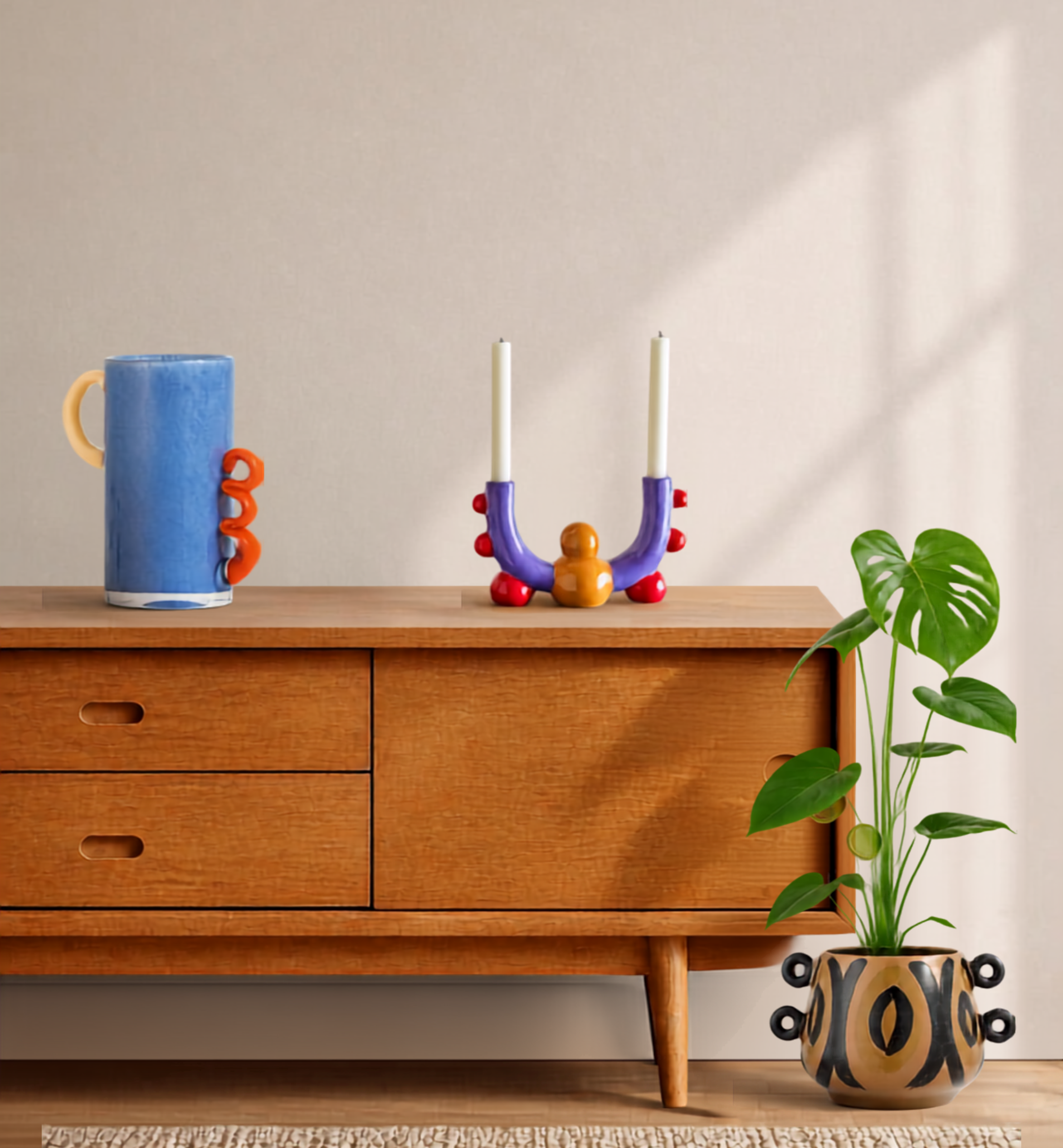 Estantería de madera con tres cajones, decorada con una planta en una maceta decorativa y un jarrón con diseño abstracto. Sobre la estantería, un vaso azul con asas y dos candelabros con velas.