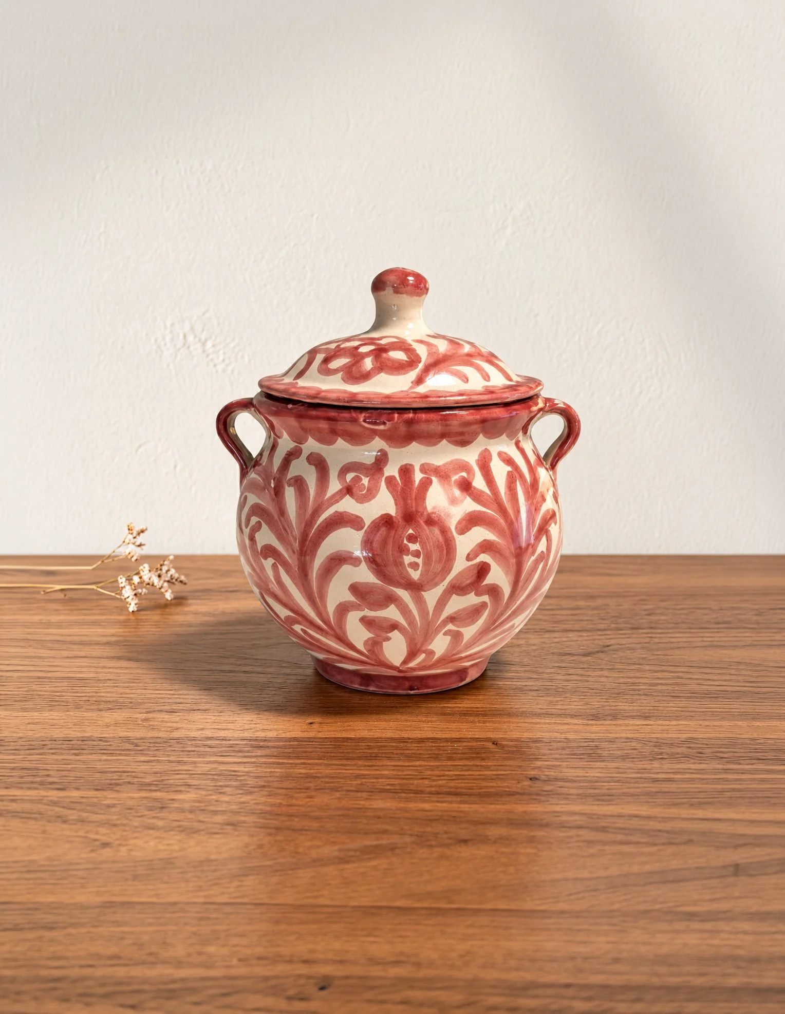 Salero o azucarero de cerámica blanco con diseño rojo en forma de flor, con tapa y asas en ambos lados, colocado sobre una mesa de madera.