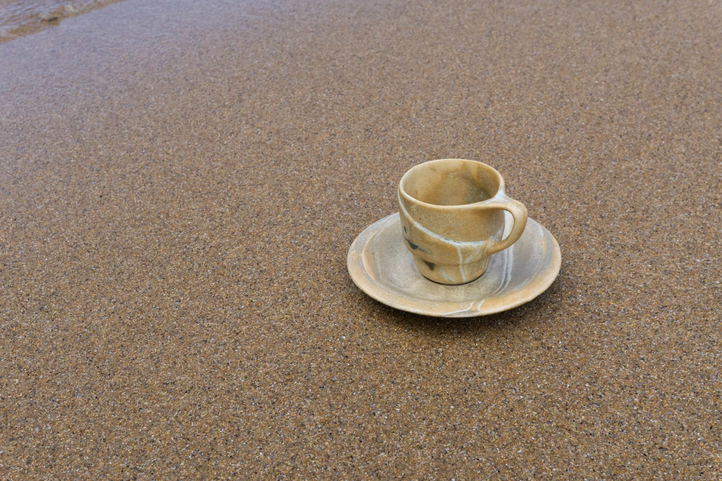 Taza de cerámica con plato sobre arena en la playa.