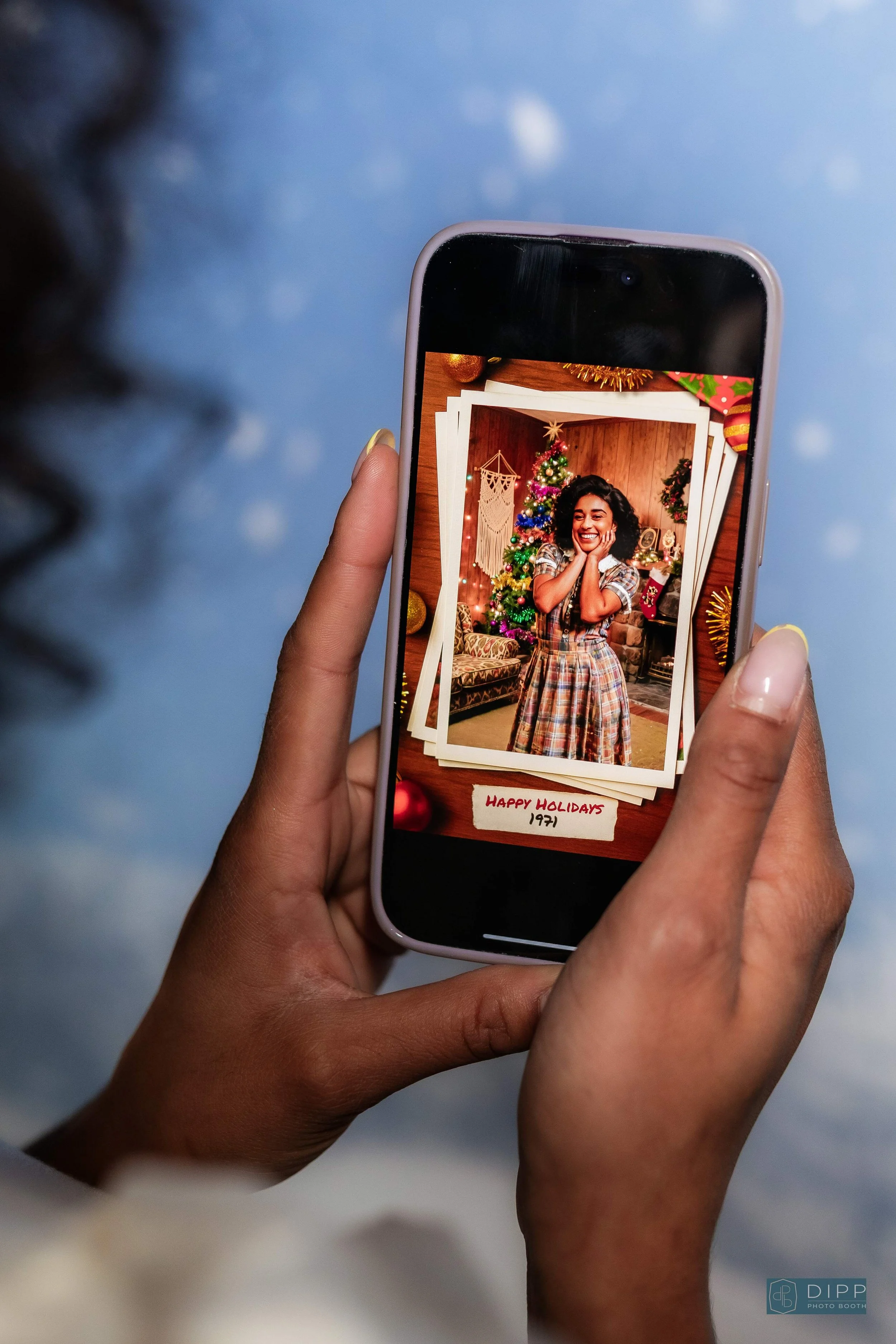A person takes a photo of a holiday-themed photo with a smartphone, showing a smiling woman in front of a decorated Christmas tree, with a note reading 'Happy Holidays 1971' at the bottom.