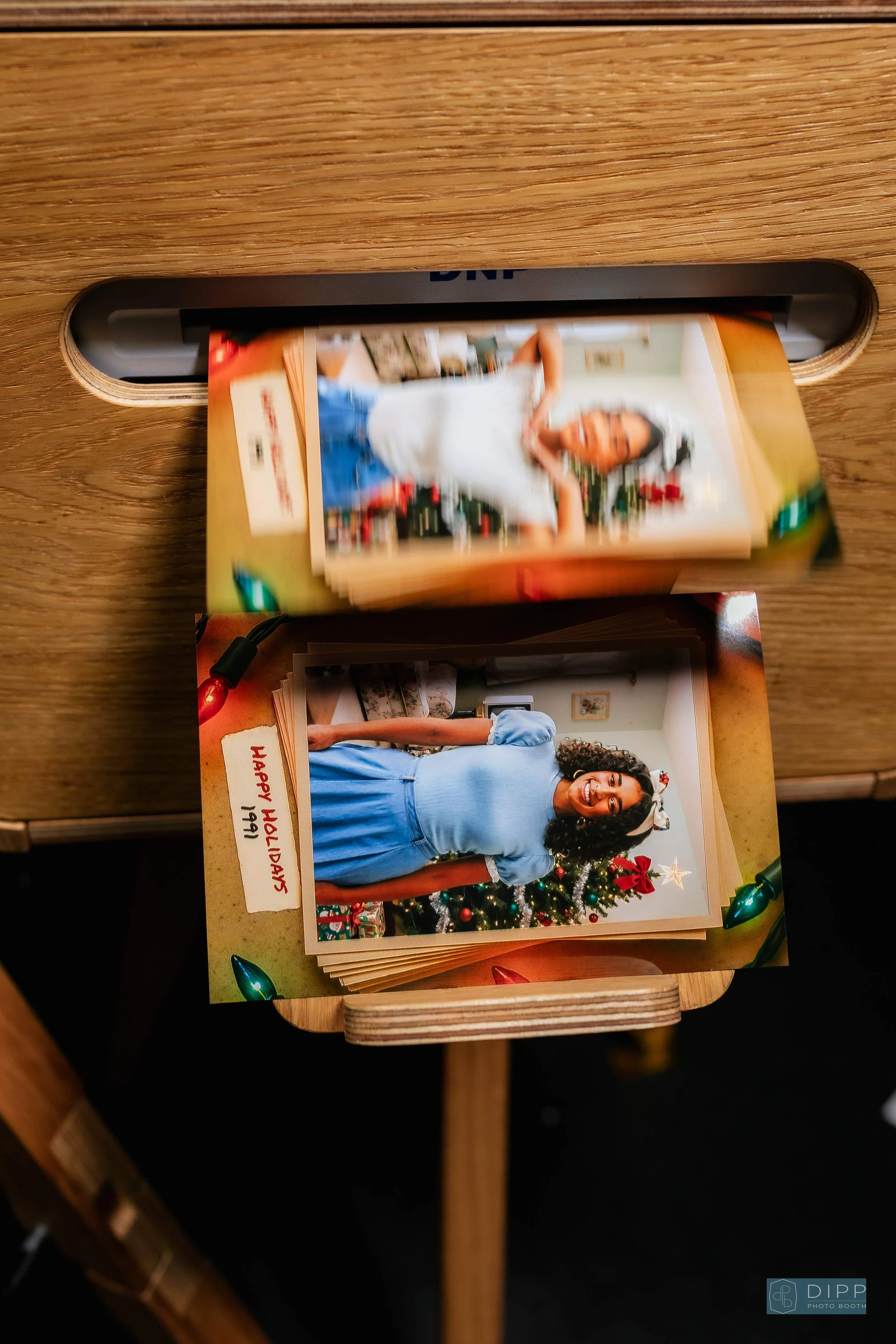 Printed holiday photo album with pictures of a woman in front of a decorated Christmas tree, labeled with handwritten notes, placed on a wooden table.