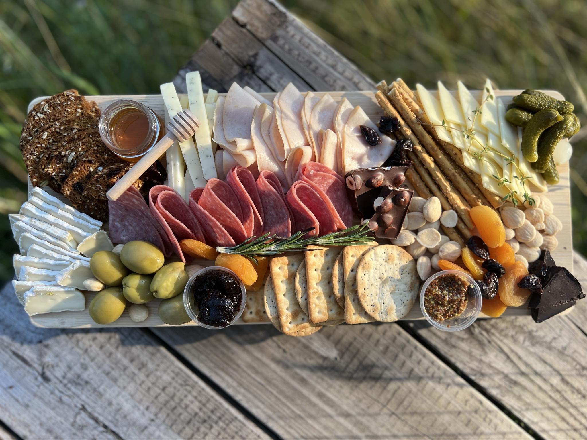 Charcuterie board with cured meats, various cheeses, crackers, bread, olives, pickles, nuts, dried fruits, honey, chocolate, fig spread, and grainy mustard.