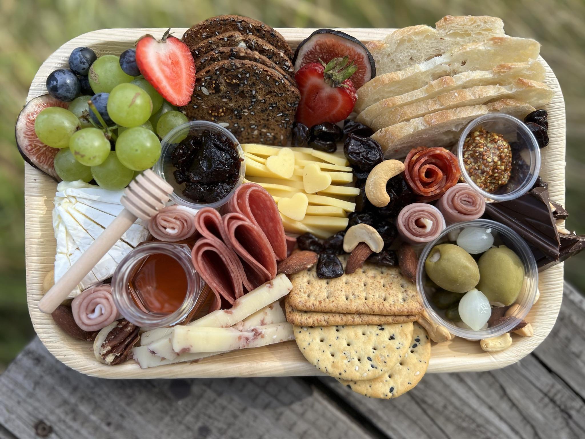 Charcuterie board from Up North Charcuterie with assorted local cheeses, meats, fruits, nuts, bread, and spreads. Includes grapes, figs, strawberries, crackers, chocolate, olives, and mustard.