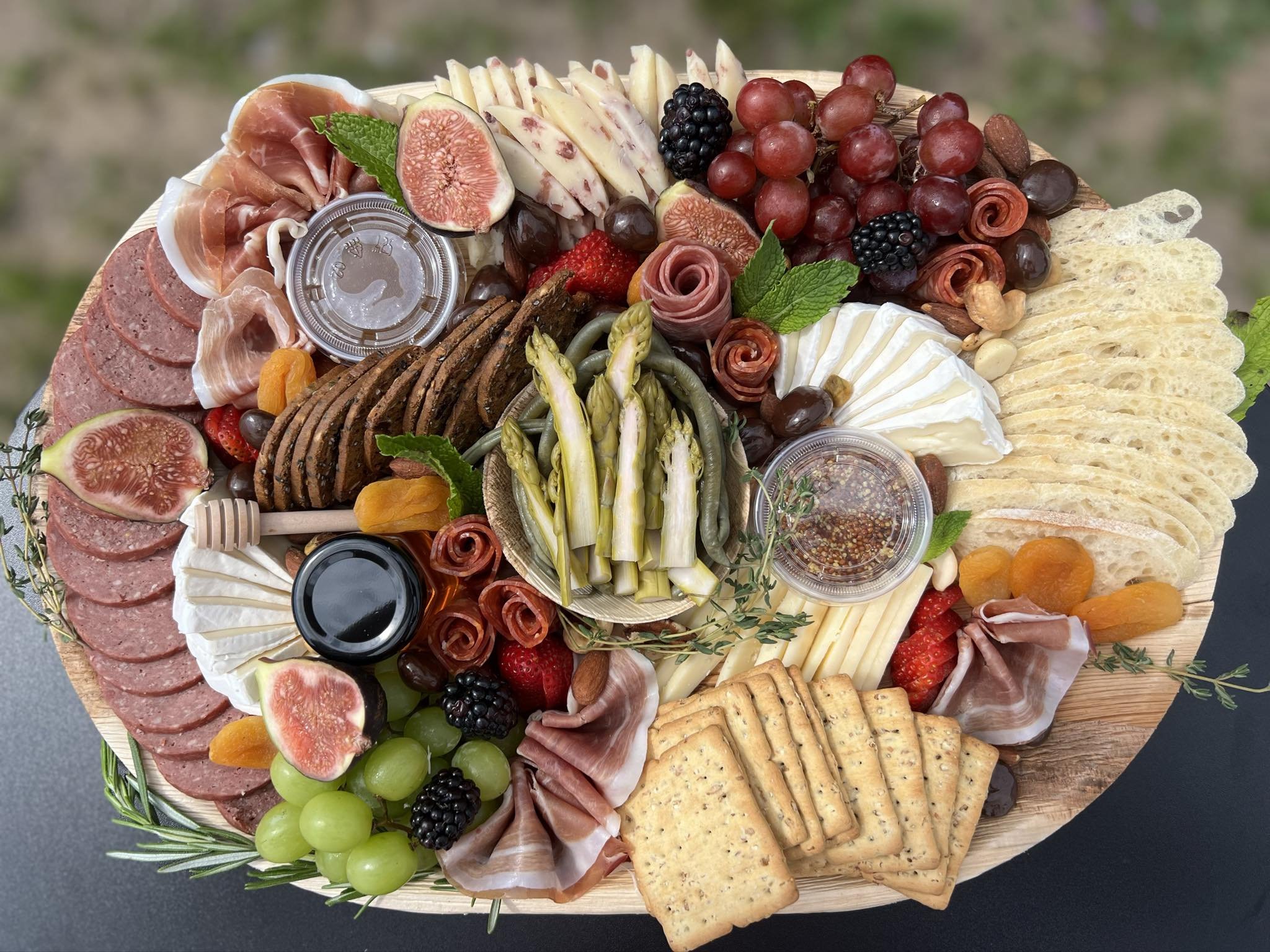 Charcuterie board with assorted meats, cheeses, fruits, nuts, and bread slices. Includes salami, prosciutto, brie, fig slices, grapes, blackberries, crackers, and spreads.