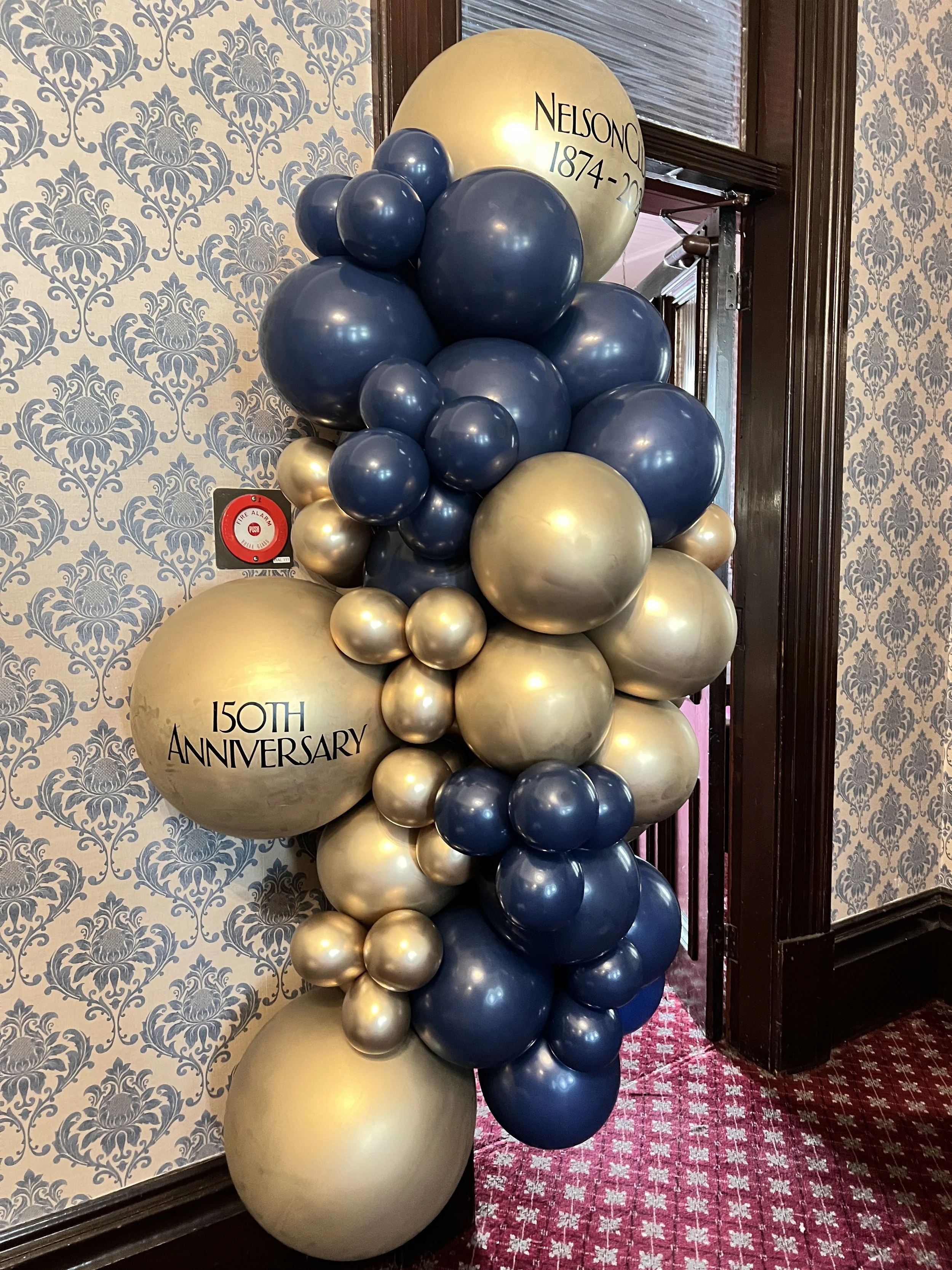 Balloon arrangement with blue and gold balloons celebrating a 150th anniversary and Nelson Corporation's 1874-2024 years.