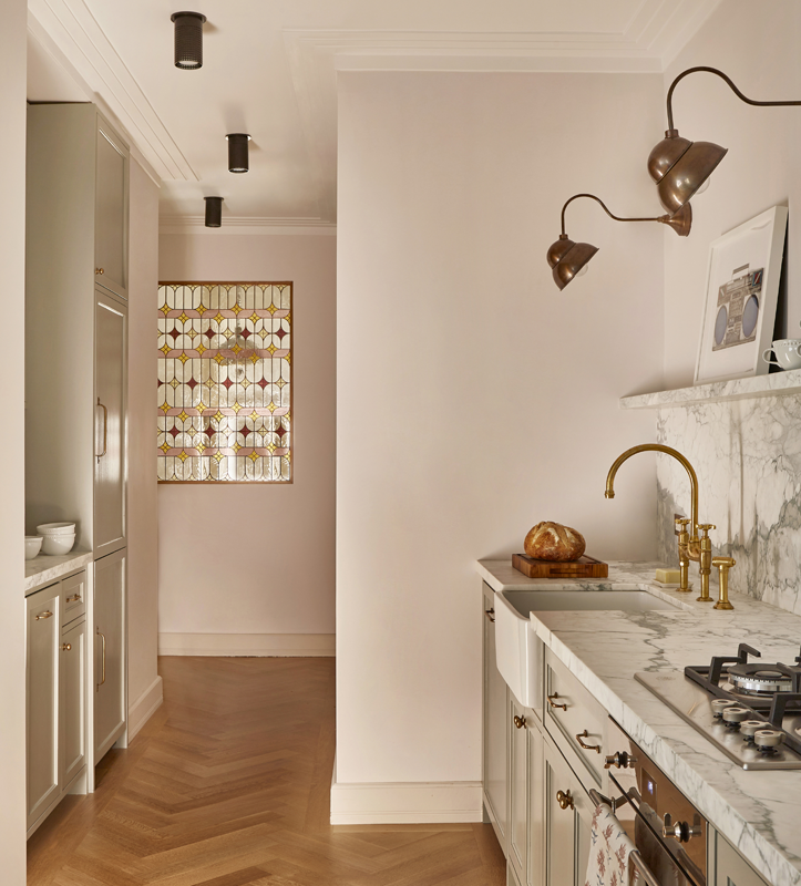 Modern kitchen with beige cabinetry, marble countertops, and brass fixtures. Includes a stove and a window with decorative stained glass. Floor is hardwood.
