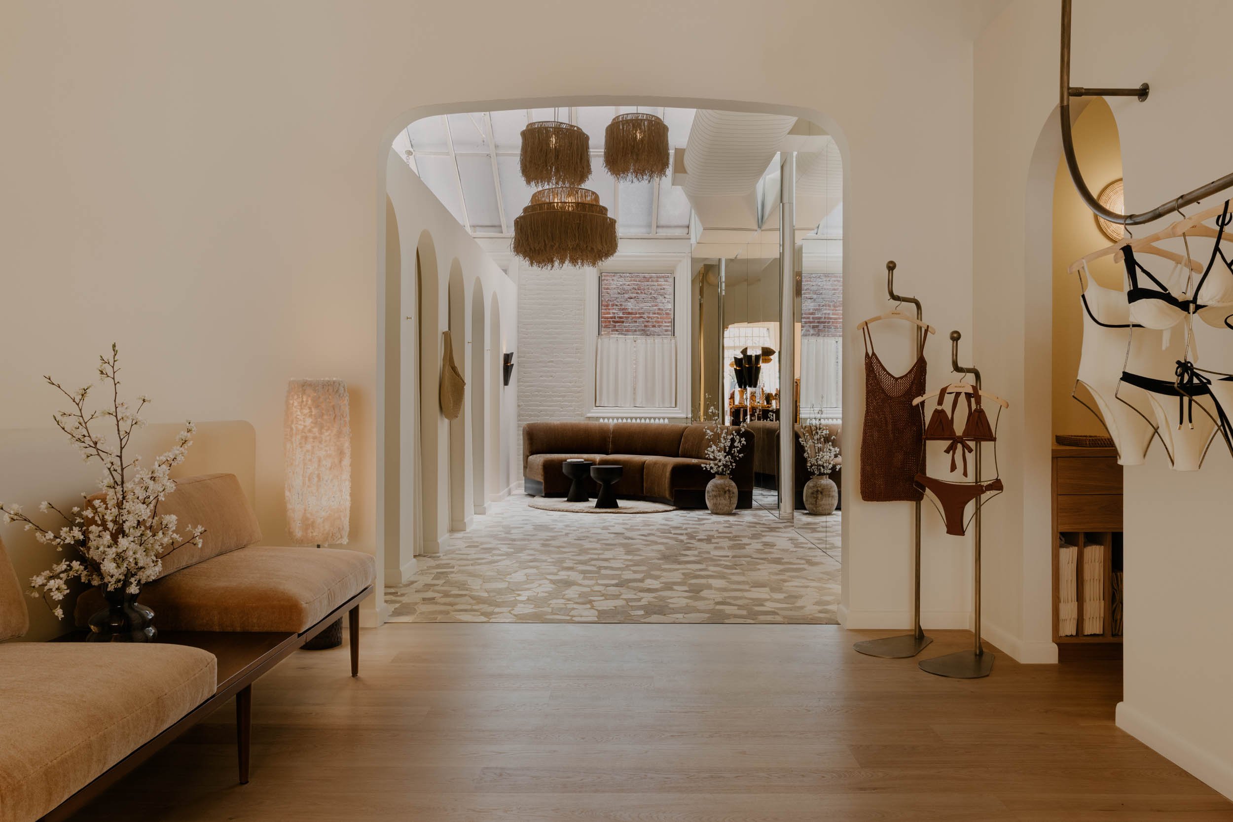 Interior of a modern living space with beige walls, hanging felt light fixtures, a brown sofa, a patterned rug, and minimalistic decor.