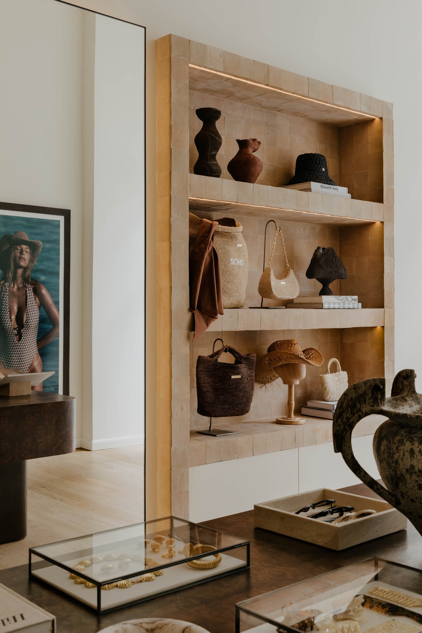A display shelf with various decorative items such as vases, handbags, books, and hats in a boutique or showroom setting.
