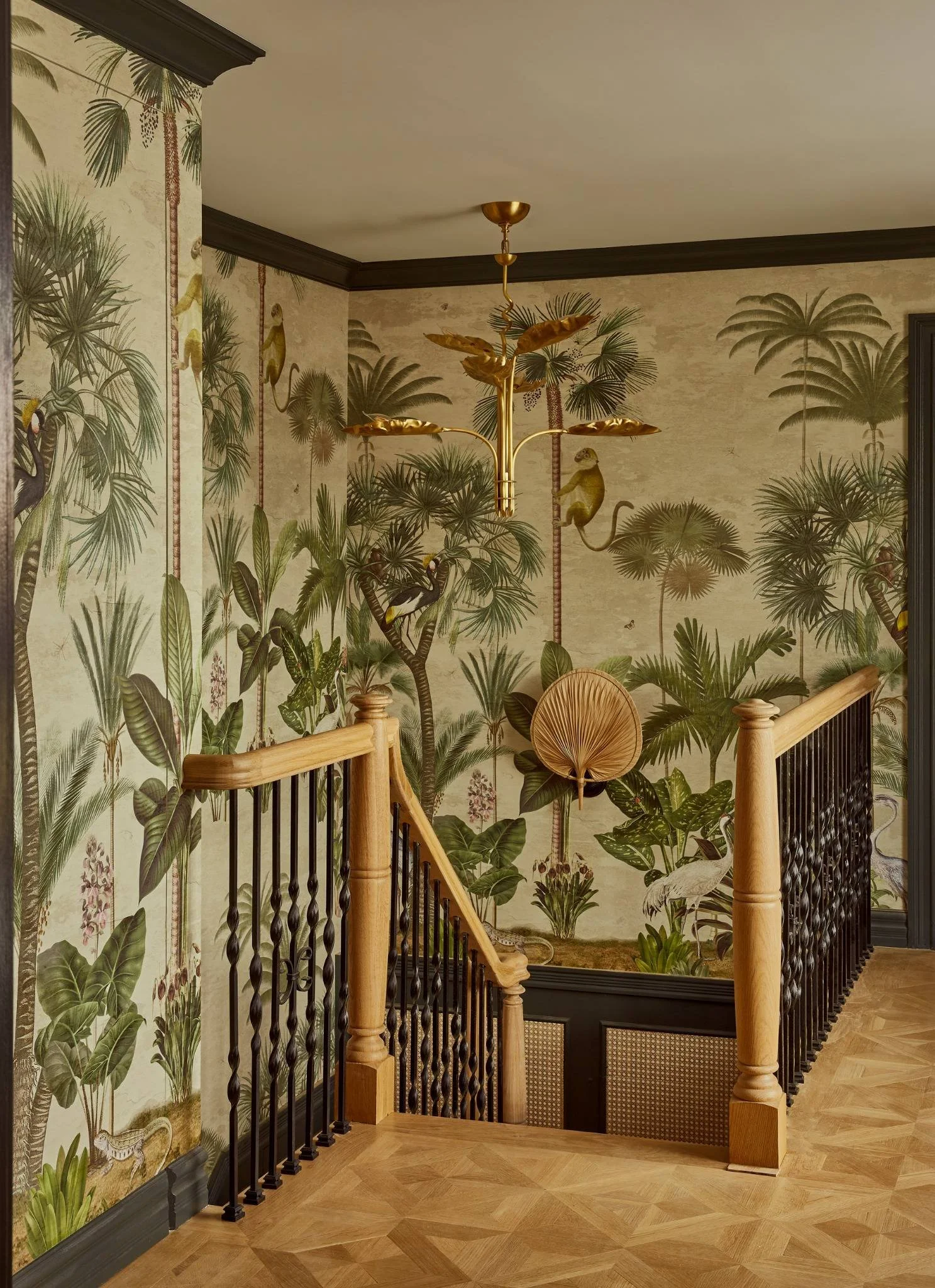 Decorative staircase with jungle-themed wallpaper featuring tropical plants, birds, and flamingos, complemented by a gold chandelier and wooden railing.