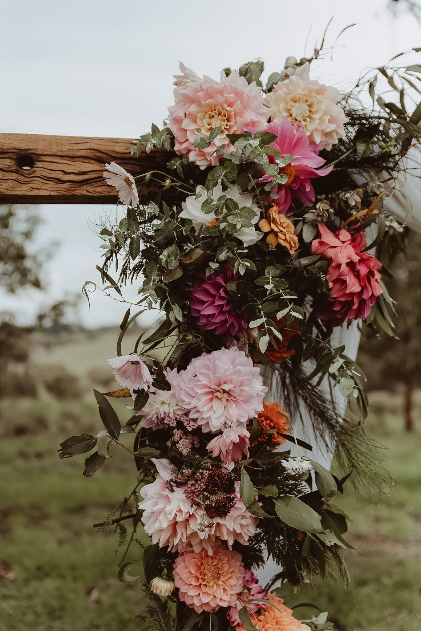 Braidwood Wedding Photographer. A vertical arrangement of various colorful flowers including pink, white, peach, and red blooms on a wooden structure outdoors.
