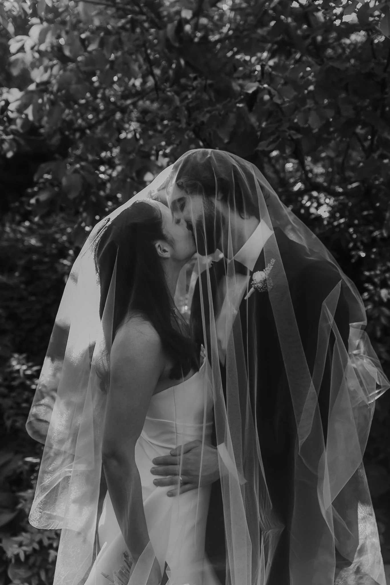 Braidwood Wedding Photographer. A bride and groom sharing a kiss under the bride's veil outdoors, with trees in the background.