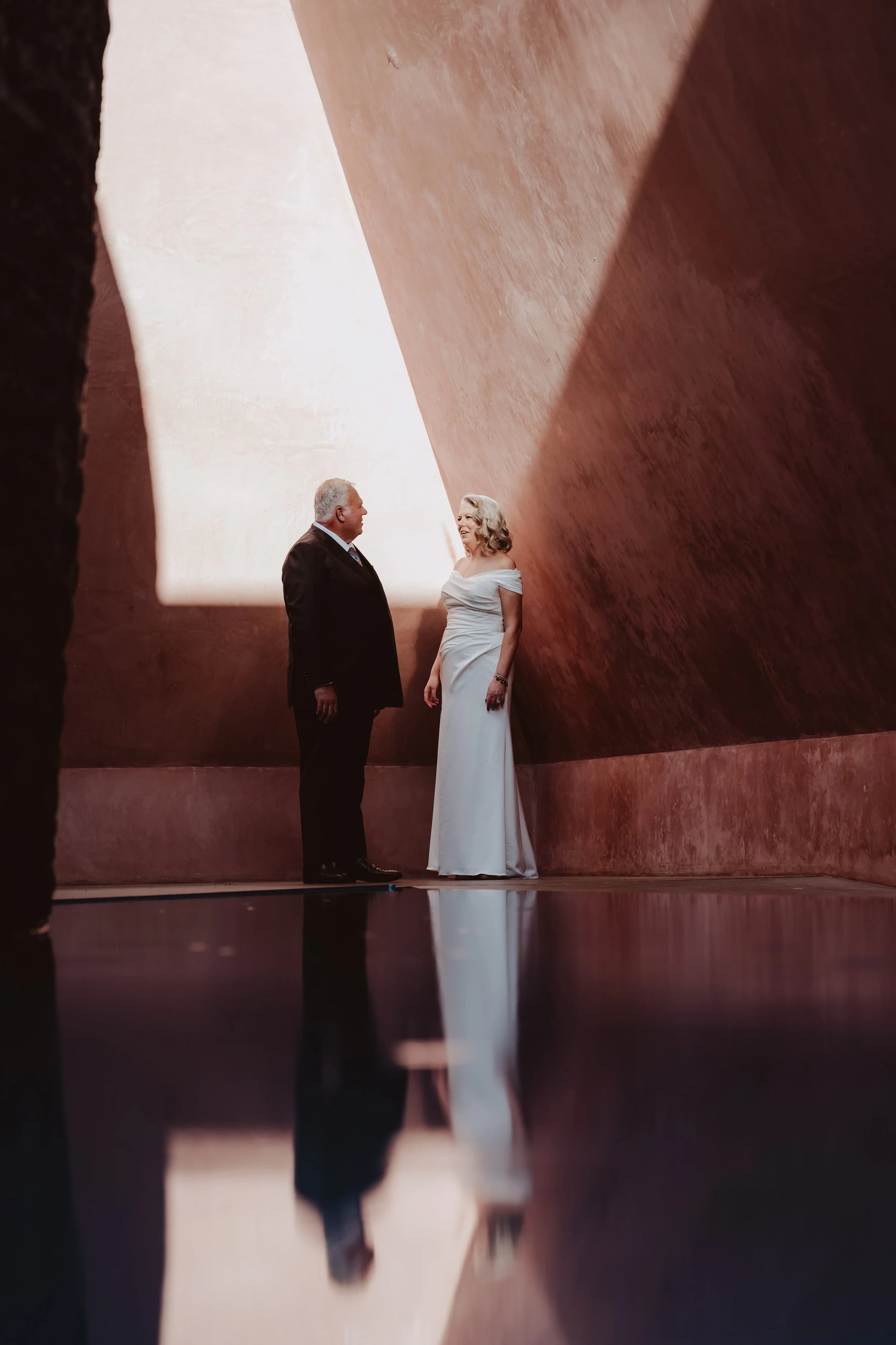 Canberra Wedding Photographer. A man and woman in formal attire standing inside a large, architectural space with curved, earth-toned walls, engaged in conversation.