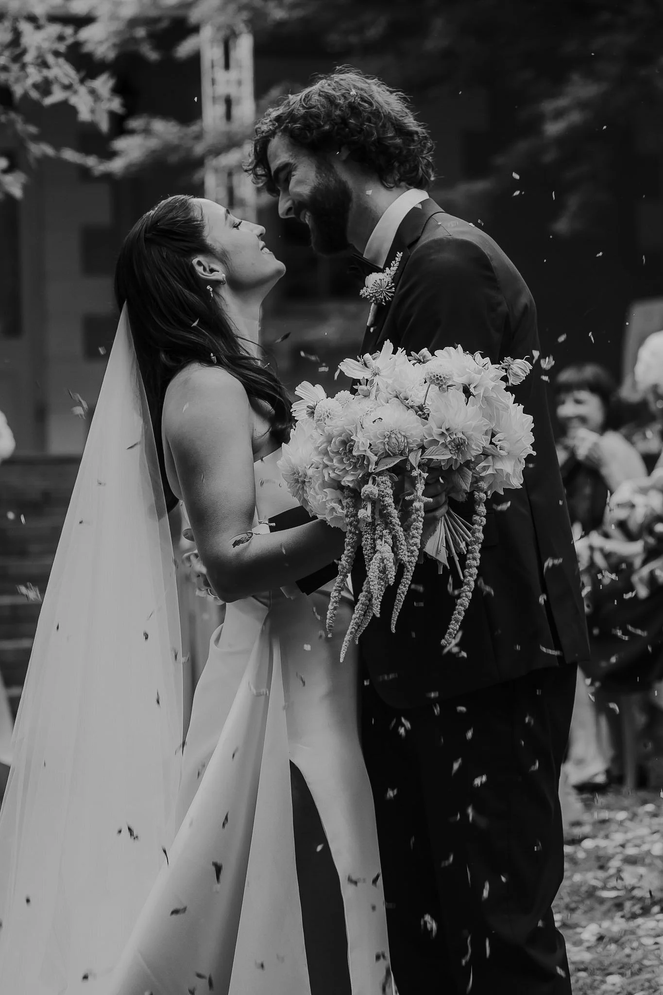 Braidwood Wedding Photographer. A bride and groom sharing a moment with their foreheads touching, holding a bouquet, during their wedding ceremony, with falling flower petals around them.