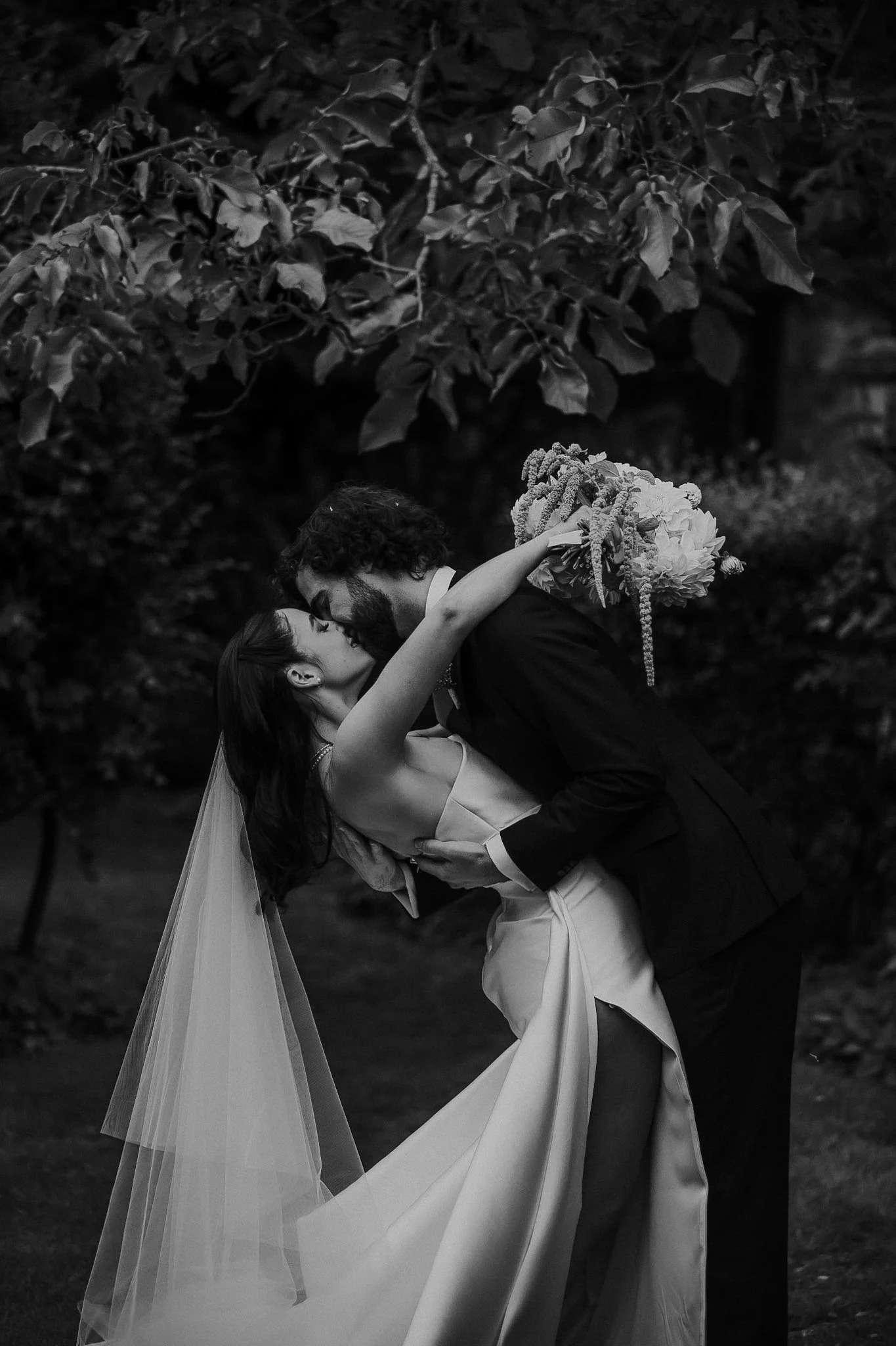 Braidwood Wedding Photographer. A couple sharing a dance outdoors, with the woman dressed in a wedding gown and the man in a suit, surrounded by trees and foliage.
