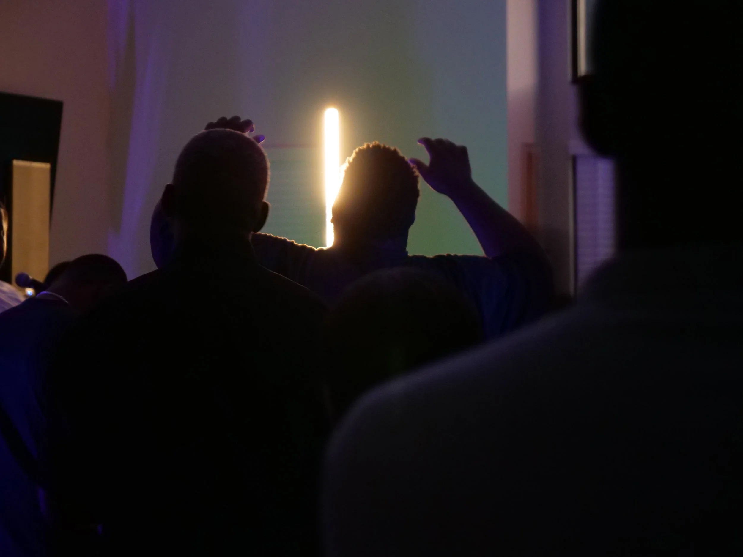 Silhouettes of people sitting in a dark room, watching a presentation or screen with a bright light in the background.