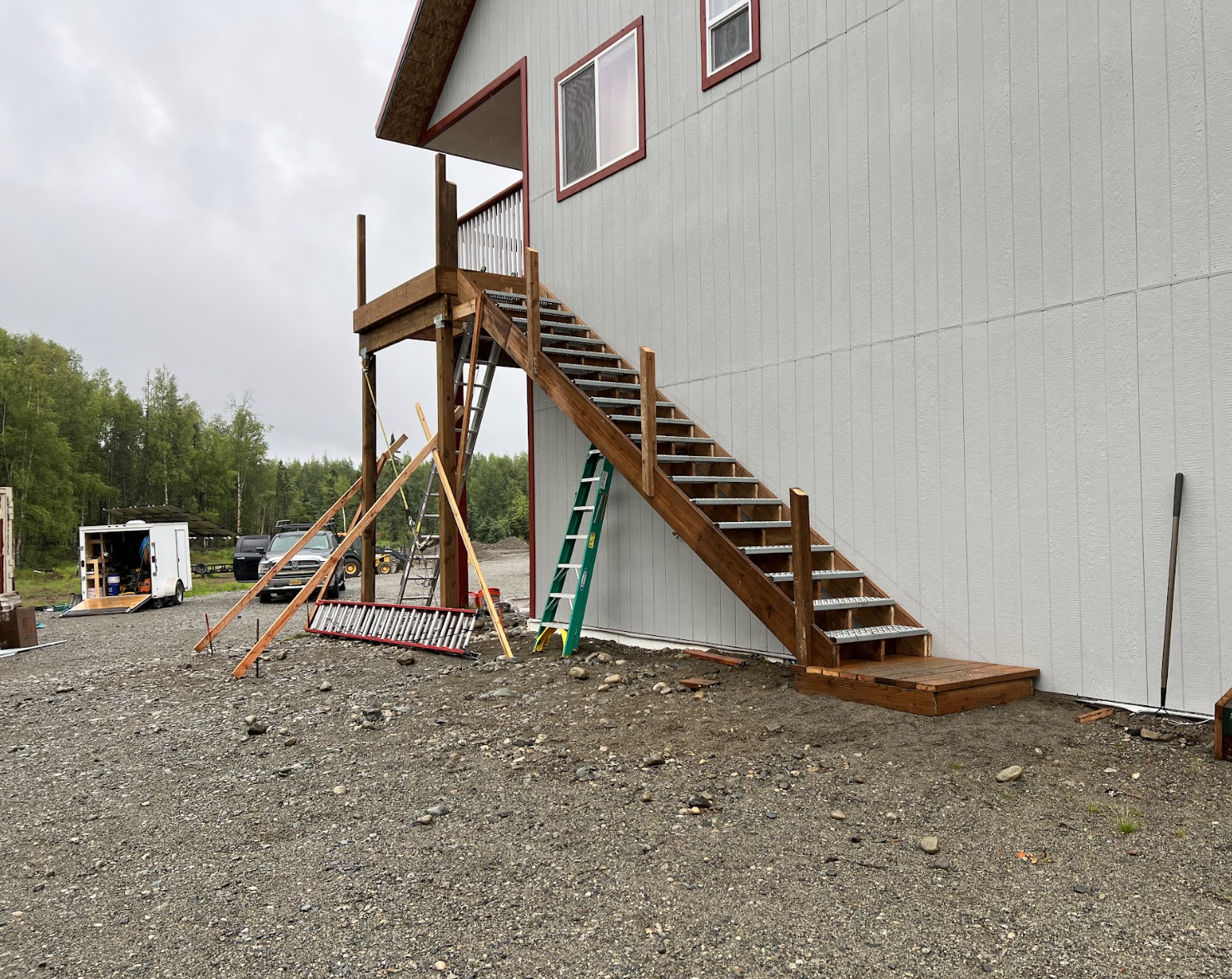 Construction site with wooden staircase attached to a gray building exterior, tools and equipment surrounding, and a gravel ground.