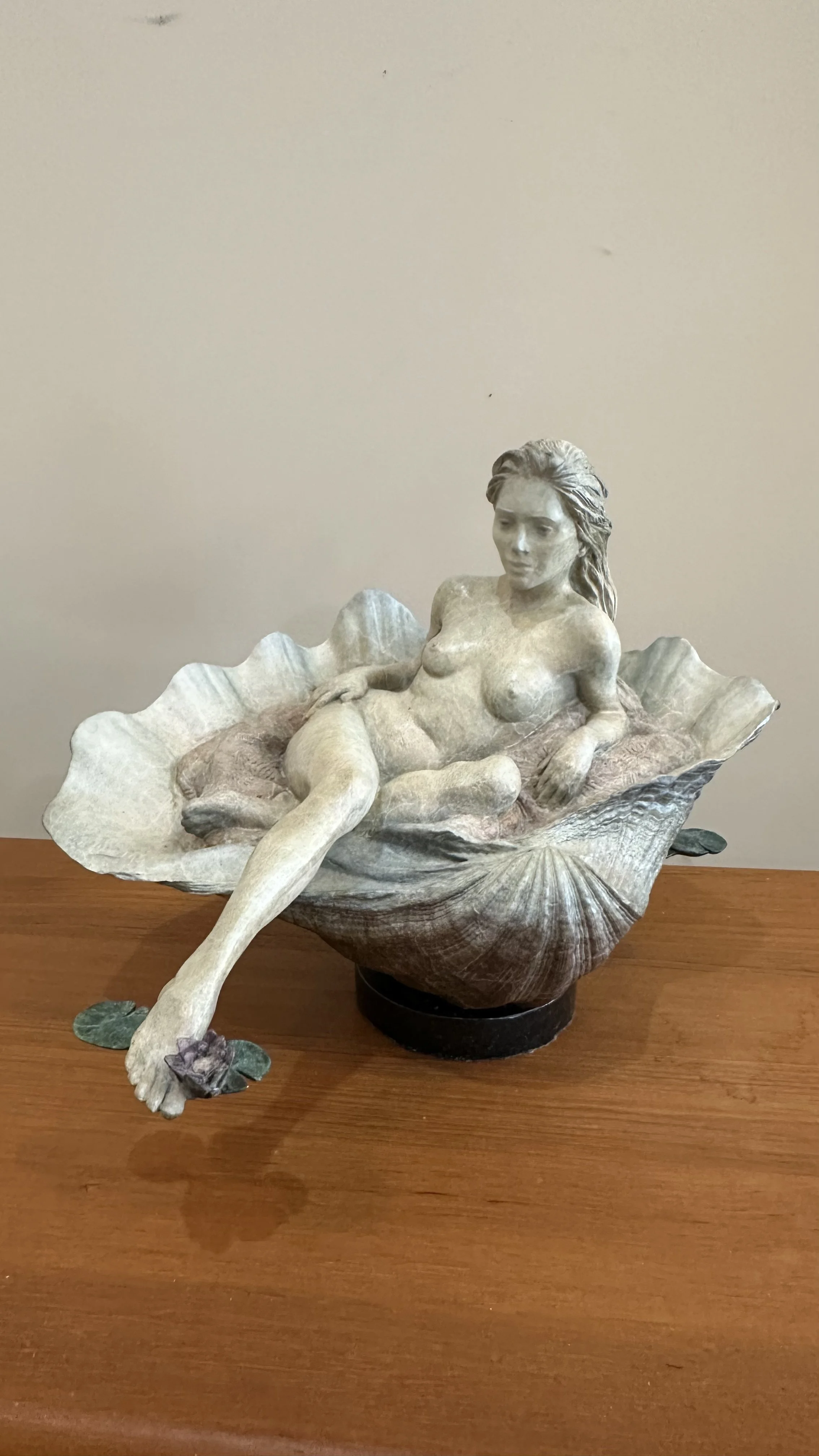 Lotus Blossom by Martin Eichinger, cast bronze figurative sculpture of a reclining nude woman resting gracefully with an open lotus blossom with soft verdigris patina.
