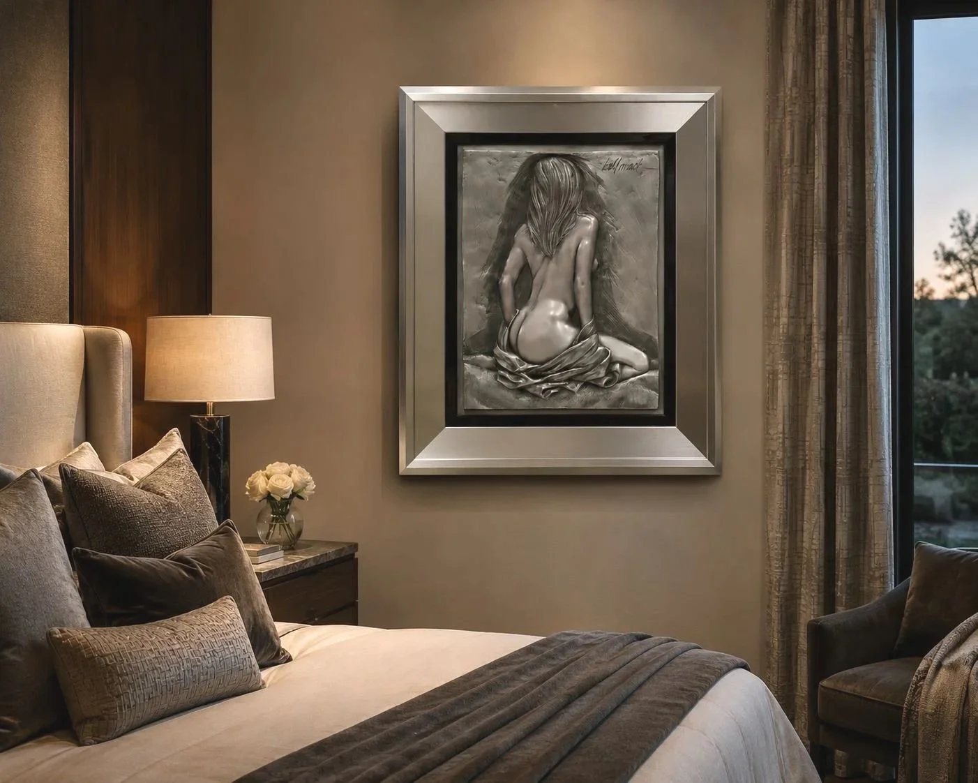 A bedroom with a bed, pillows, a bedside lamp, a small vase with white roses on a nightstand, and a large framed black and white artwork of a woman with long hair from behind hanging on the wall next to a window with curtains.