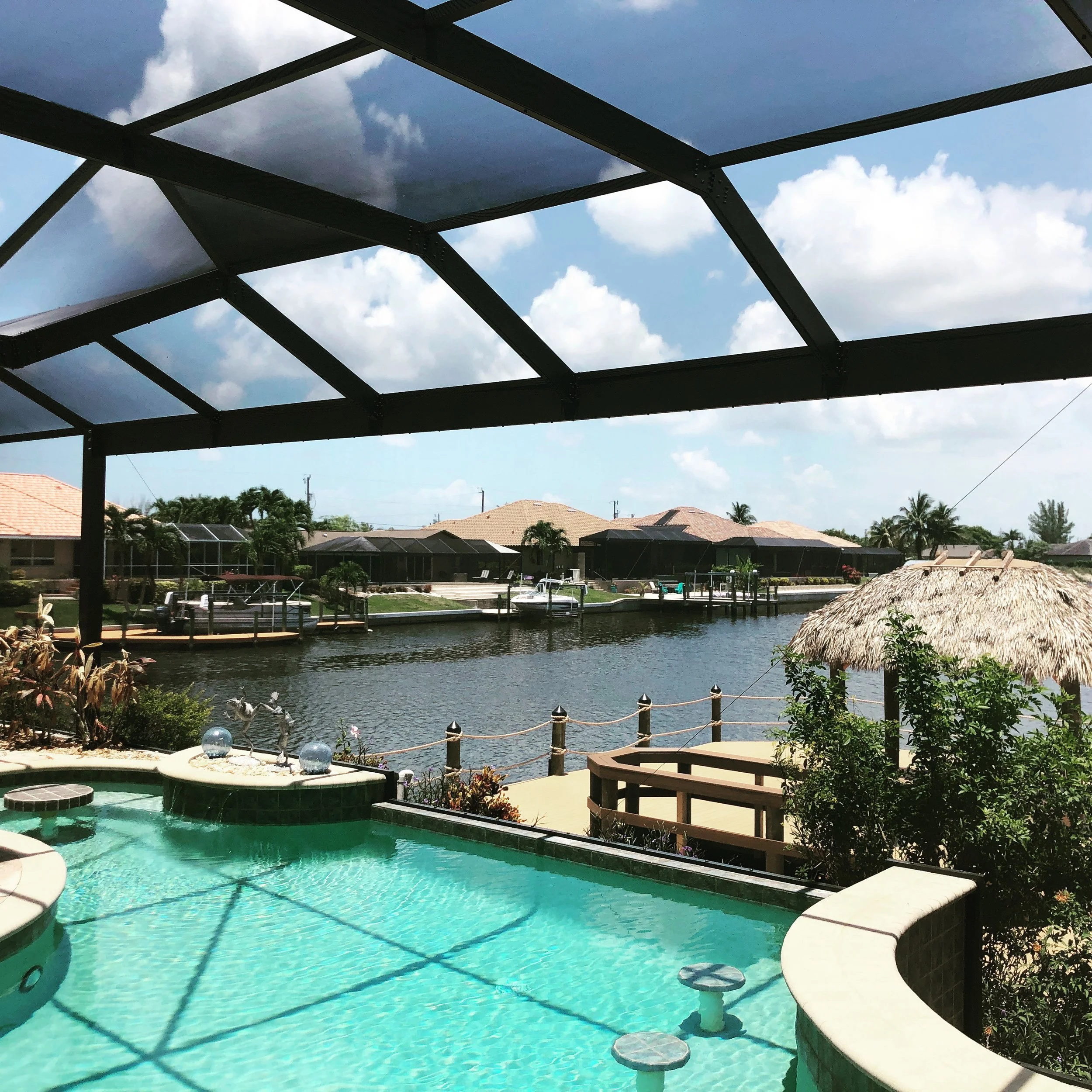 View of a backyard pool area under a screened patio with a view of neighboring houses, landscaped lawn, and a cloudy sky.