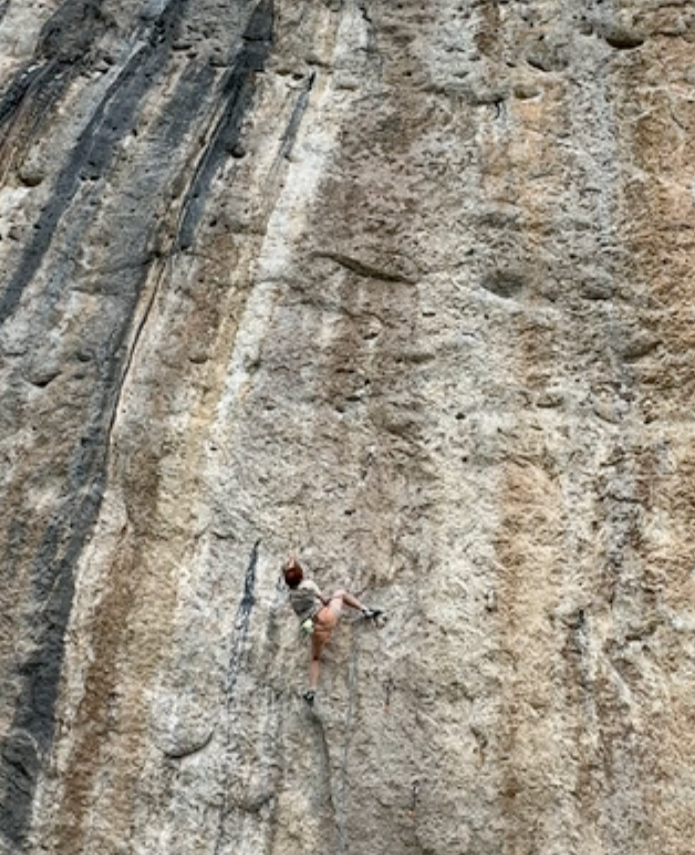 Person rock climbing on a large, beige, textured rock wall outdoors.