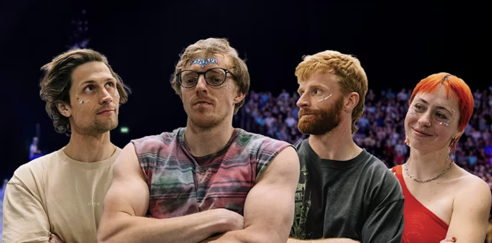 Four people stand together at a crowded event, with stage lighting and audience in the background. They have decorated faces and casual clothing, indicating a festive or celebratory atmosphere.