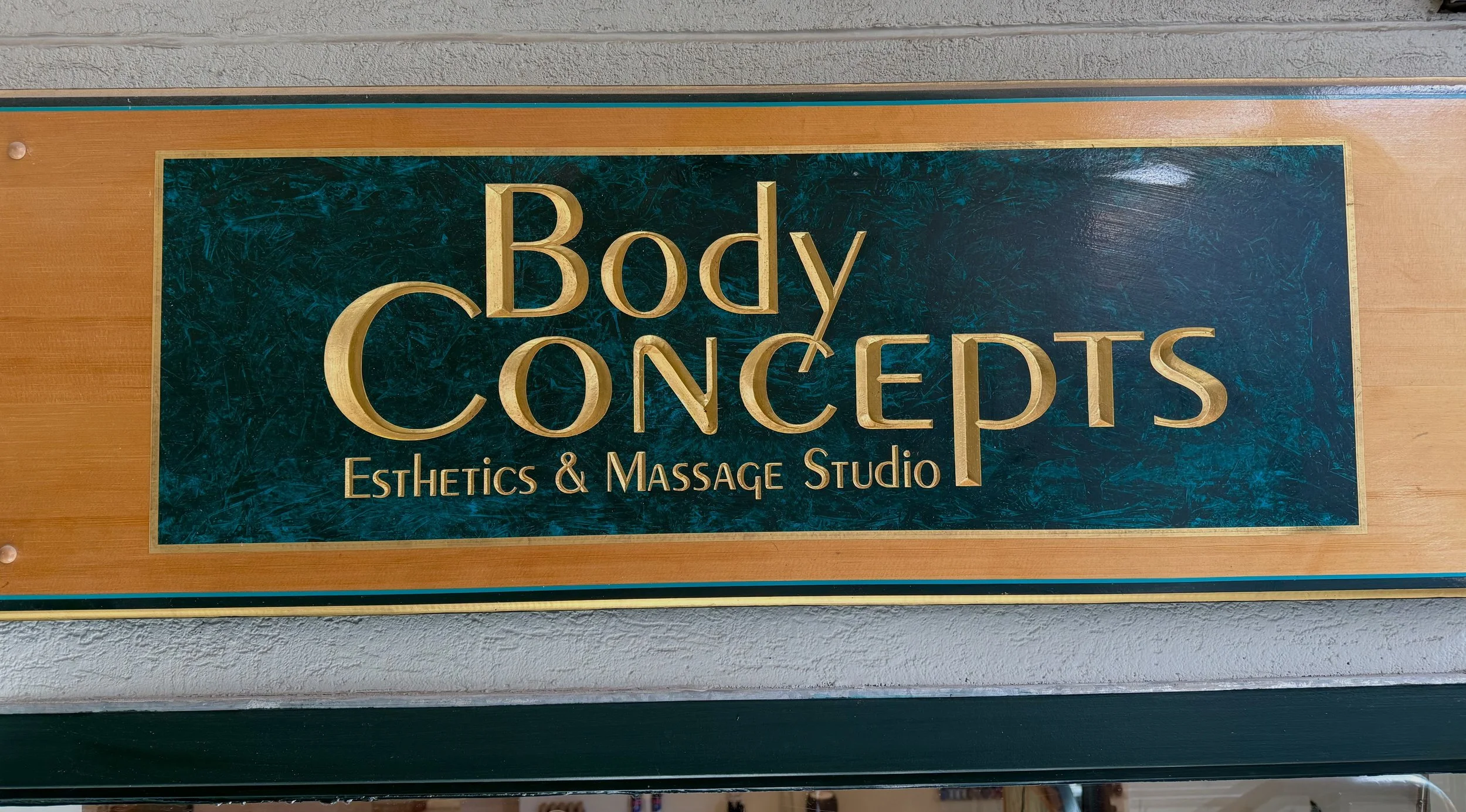 Sign for Body Concepts Esthetics & Massage Studio with gold lettering on a dark green marble background.