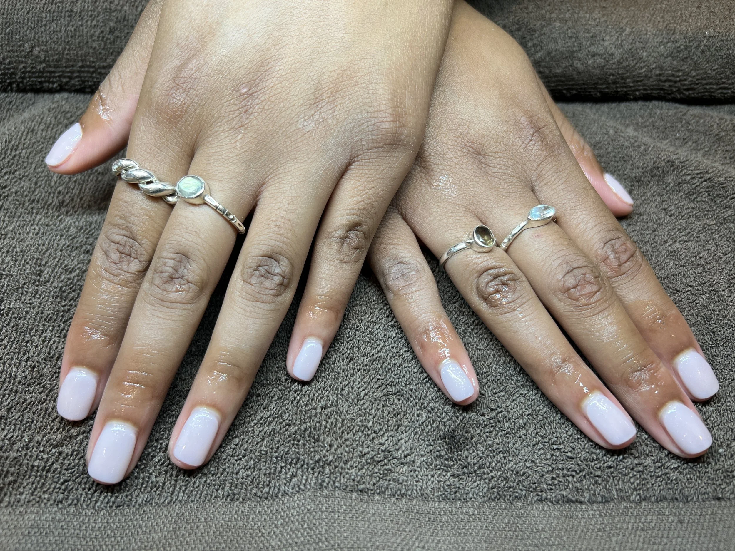 Two hands with manicured nails resting on a brown fabric surface, each hand wearing a silver ring with a circular gemstone.