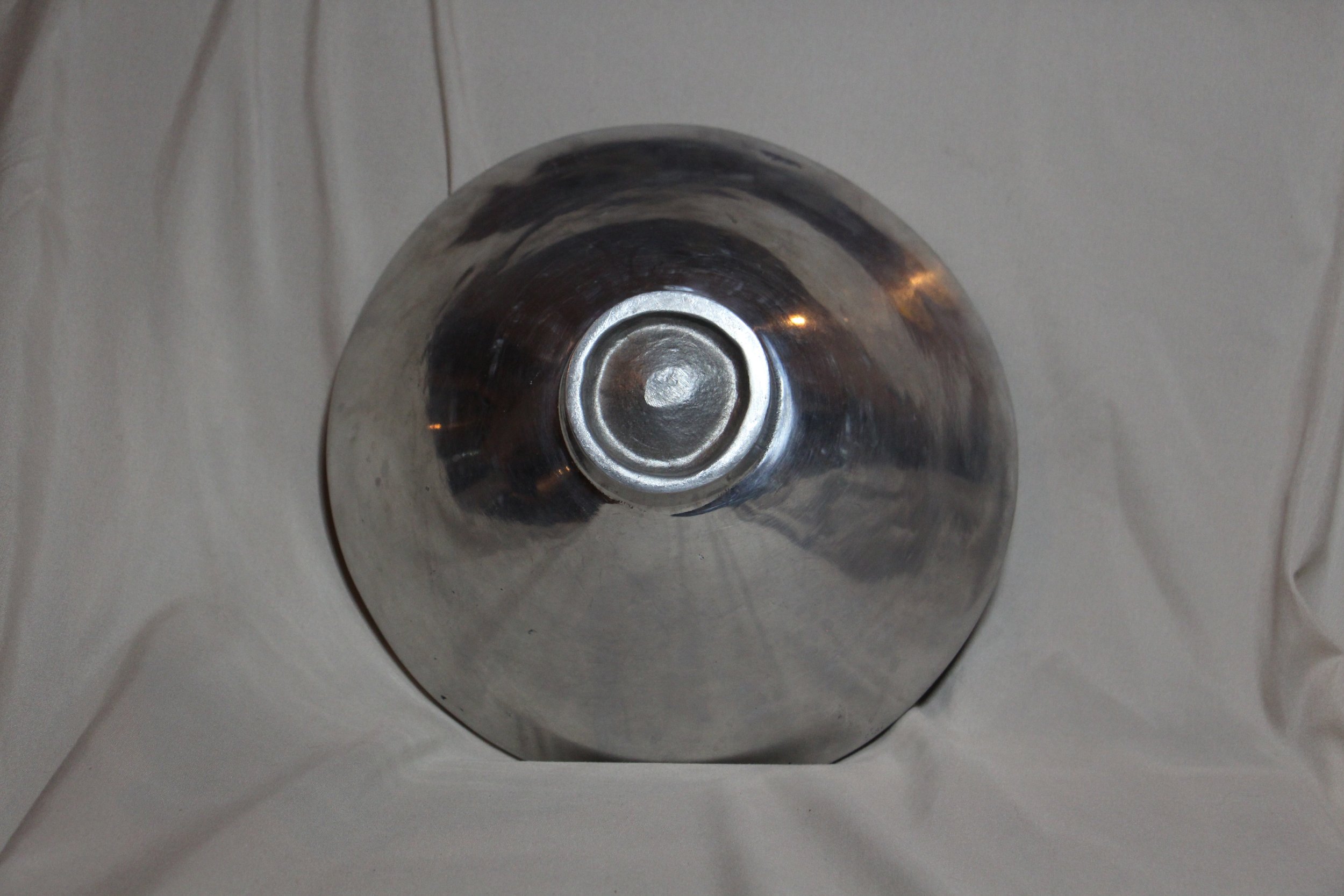 A shiny, metallic, spherical object with a circular indention at the top, placed on a white fabric background.