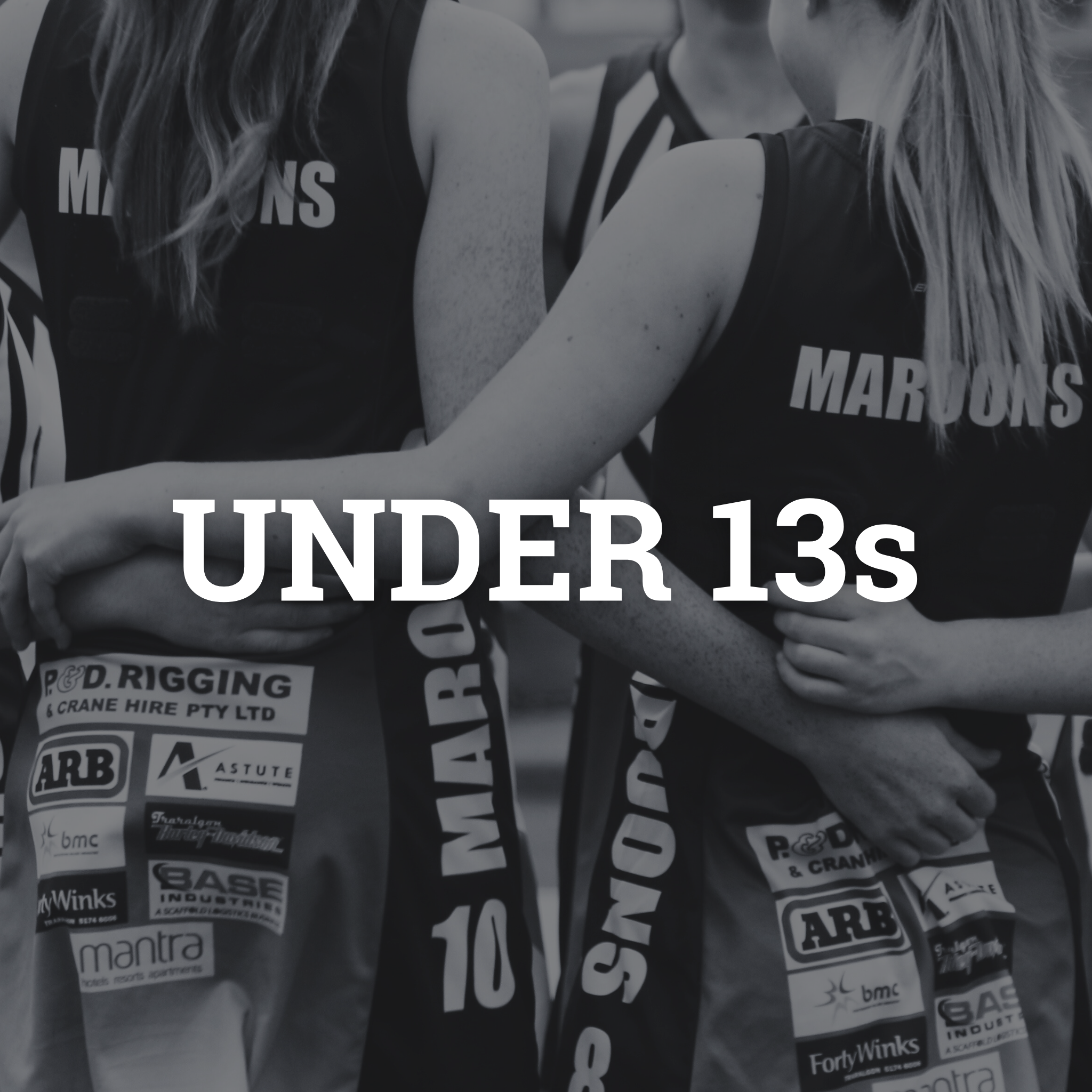 Two girls in sports uniforms hugging with their arms around each other, showing team sponsorship logos on their shorts, taken in black and white.