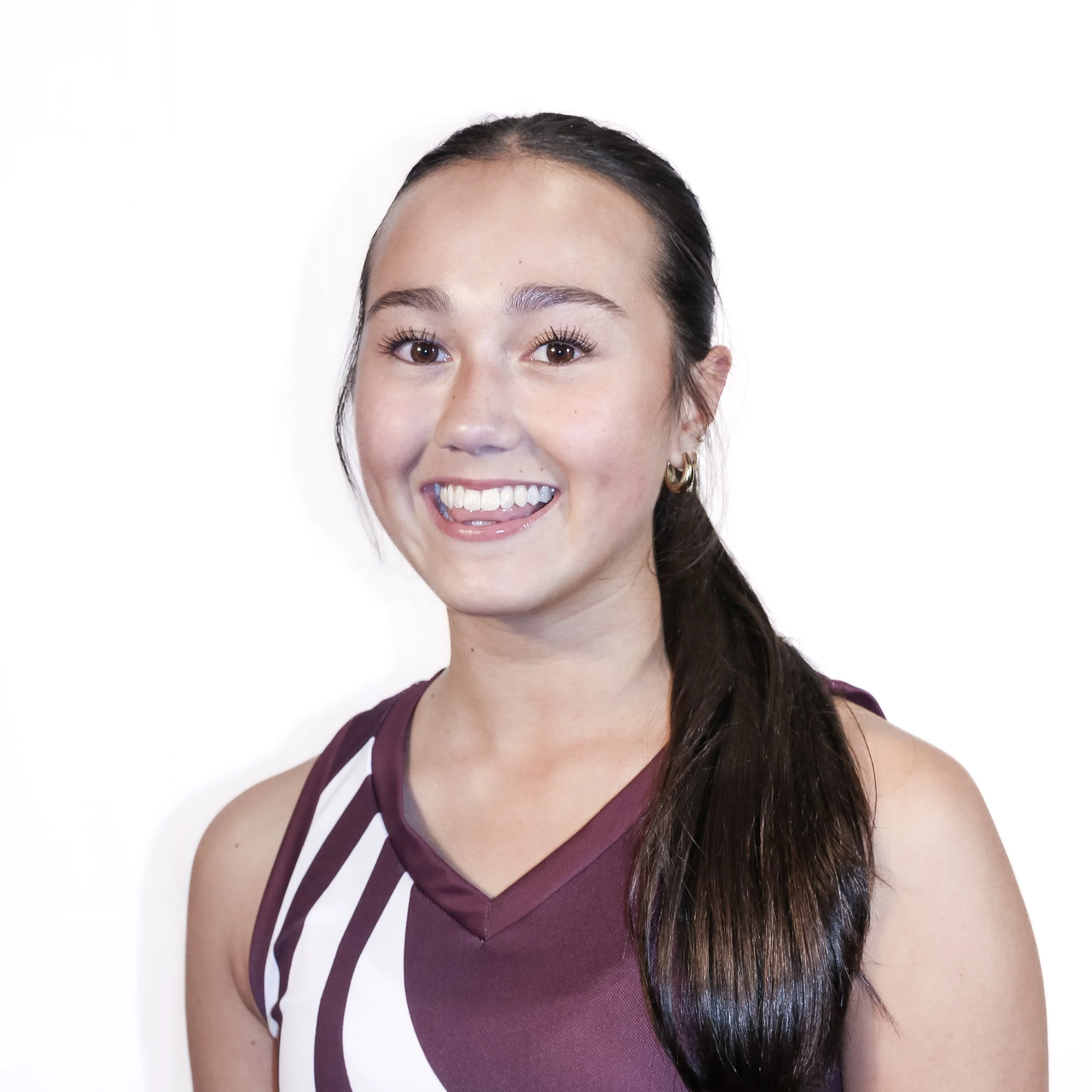 Close-up of a woman's face with long dark hair, smiling, wearing a maroon sleeveless top with white trim, against a plain white background.