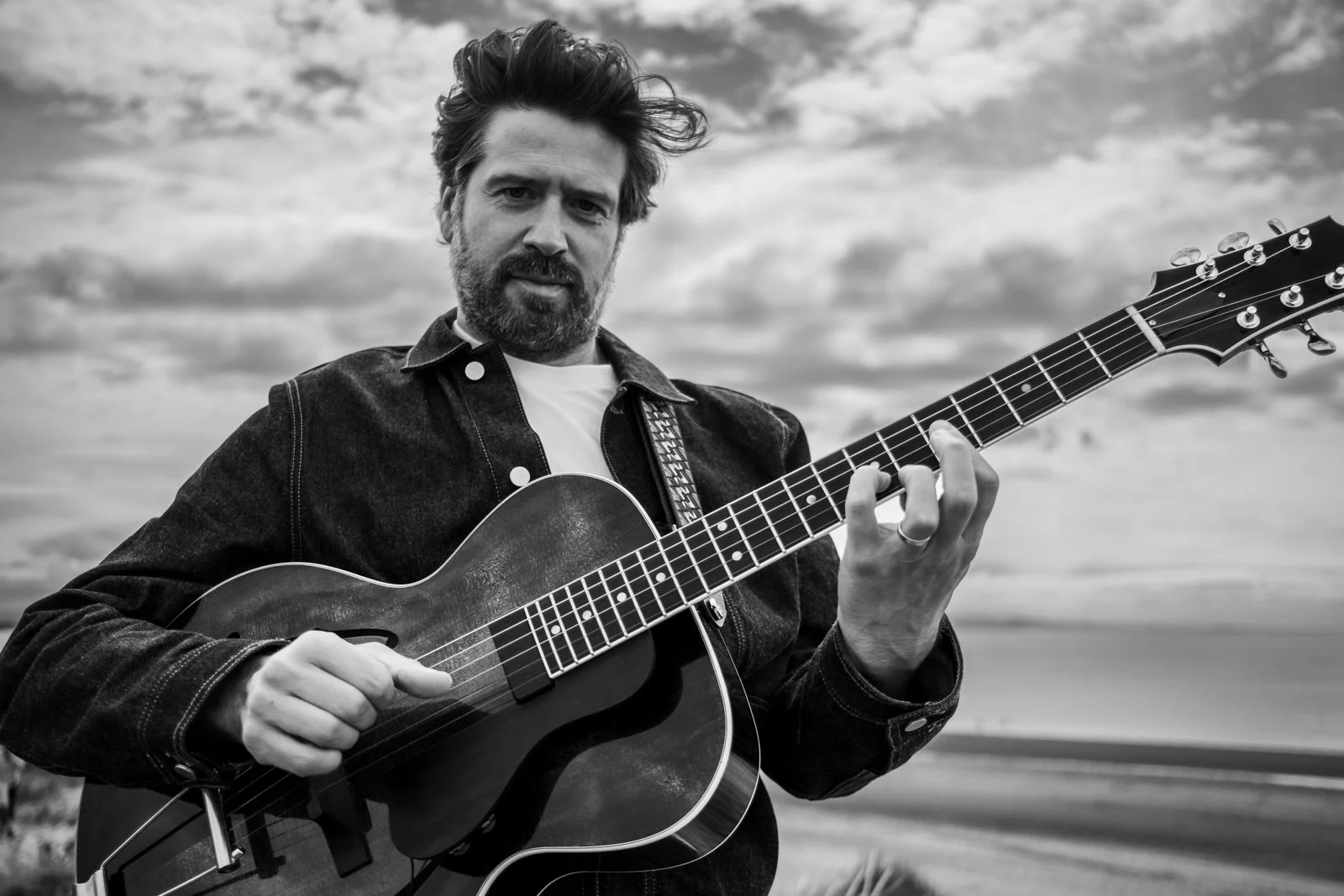 Black and white photo of a man playing an acoustic guitar outdoors.