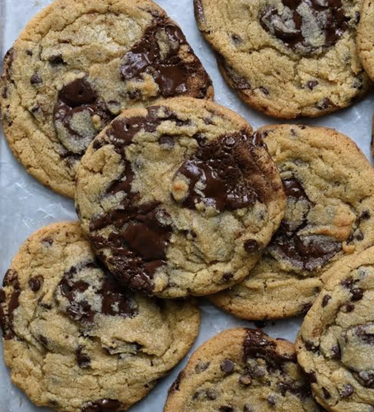 A group of freshly baked chocolate chip cookies with melted chocolate, placed on parchment paper.