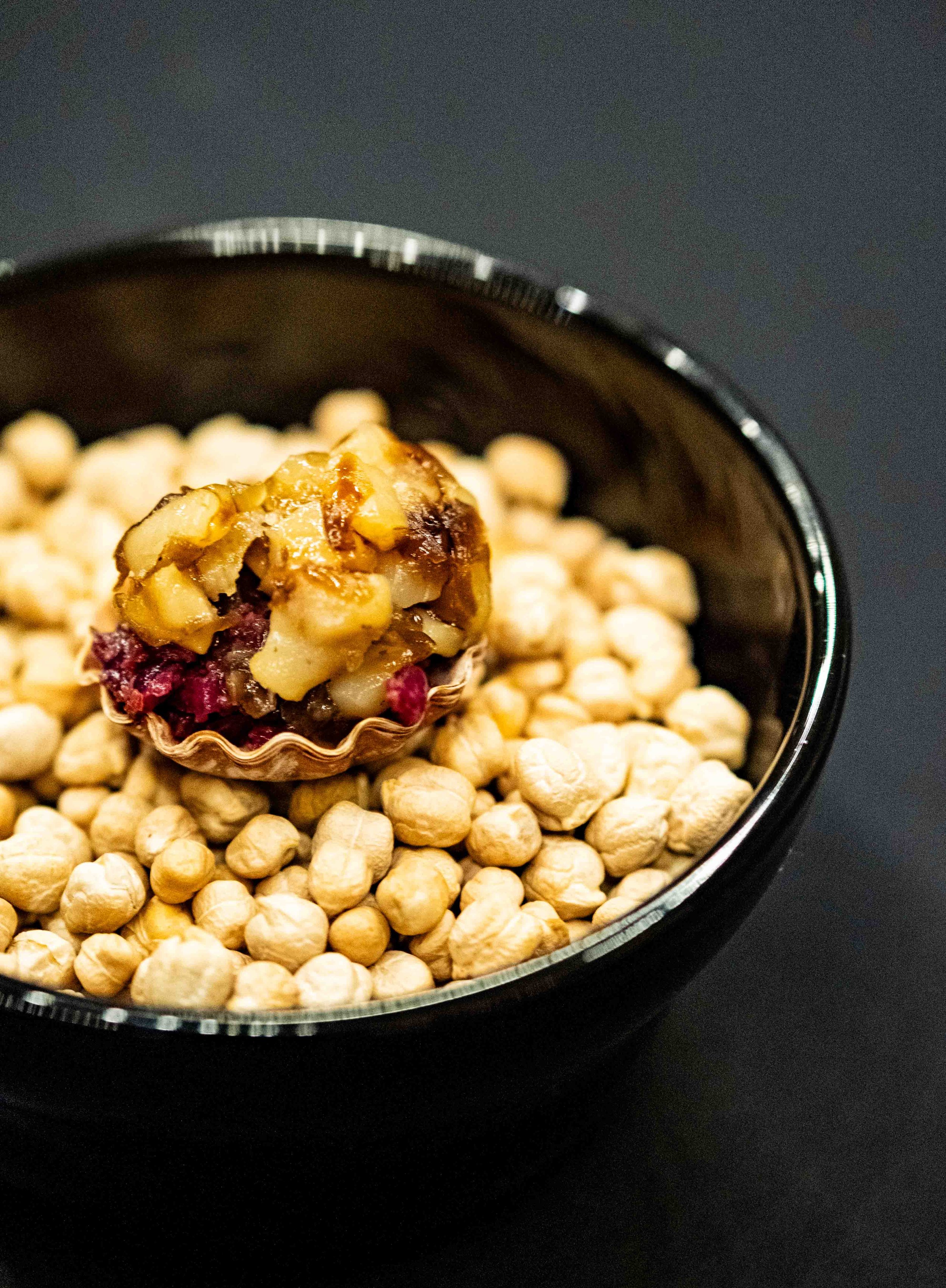 A spoonful of chunky fruit compote or tart resting on a bed of dried chickpeas in a black bowl on a dark surface.