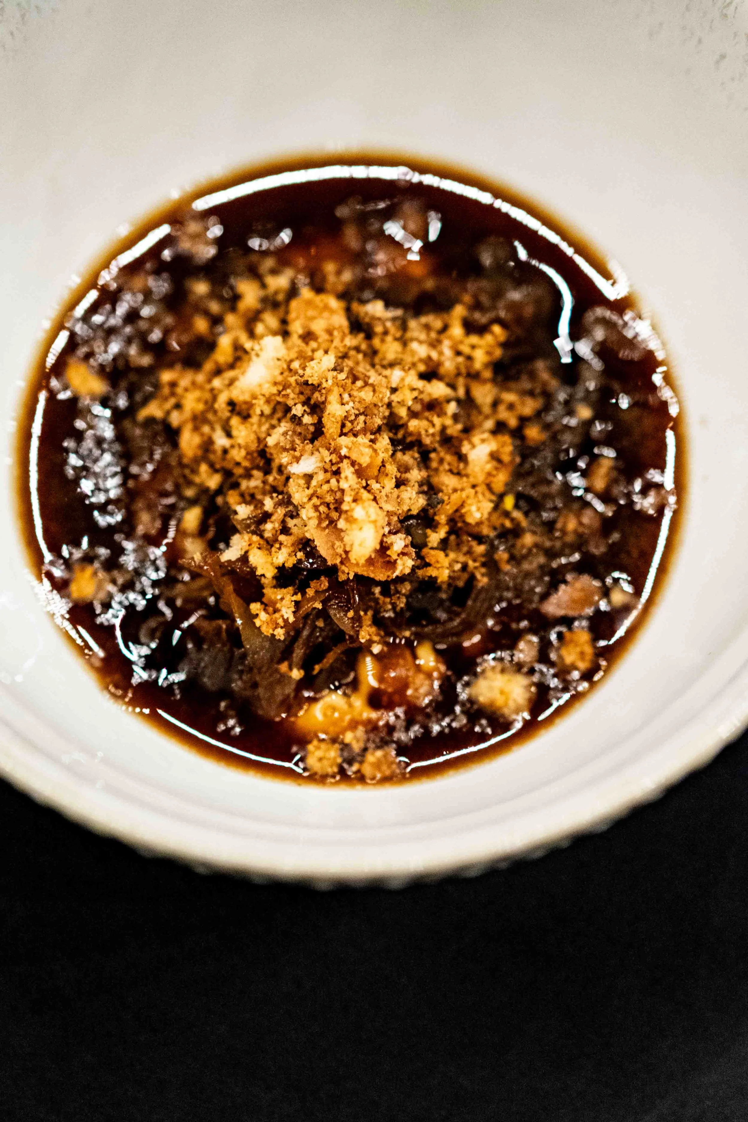 Close-up of a dessert topped with crumbled cookies in a white bowl on a black surface.