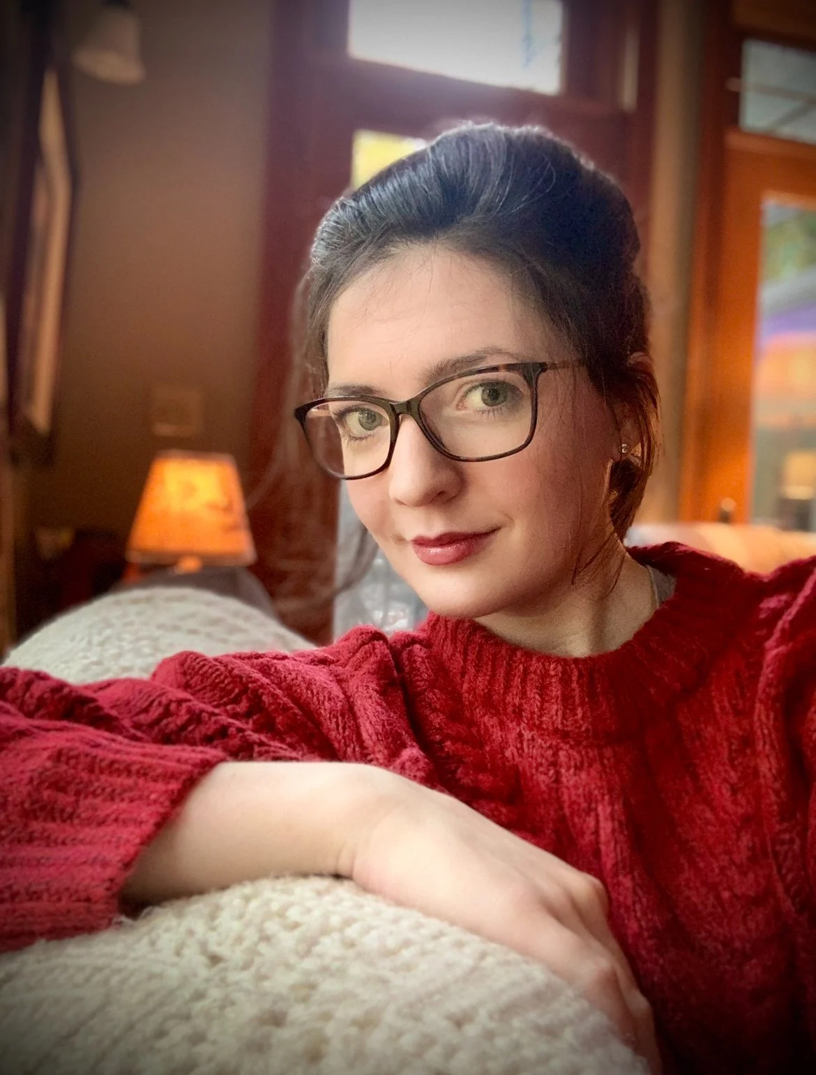 White Woman wearing a red jumper with brunette hair and glasses and a bold lip