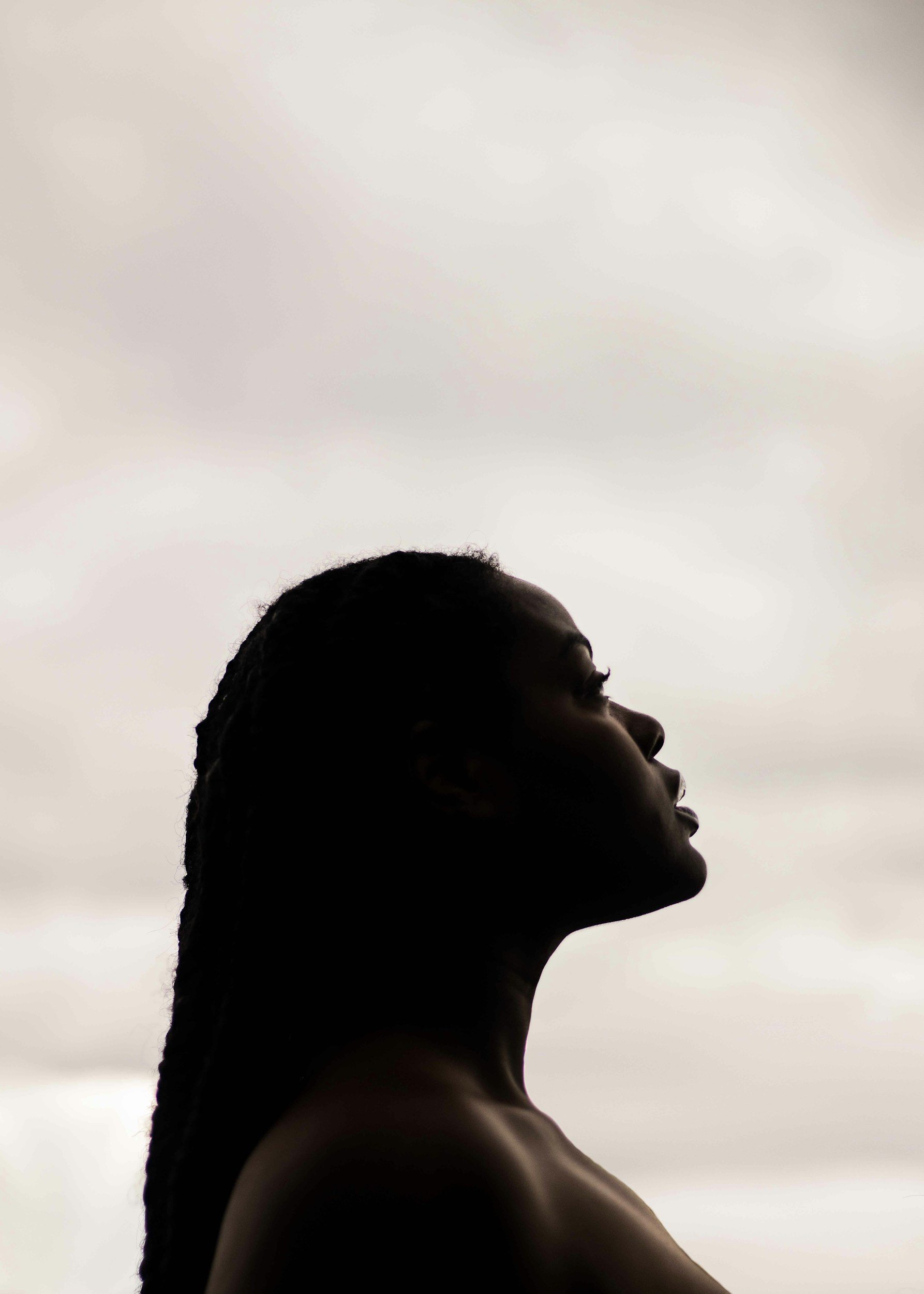 Silhouette of a woman with long hair looking upwards against a light sky background.