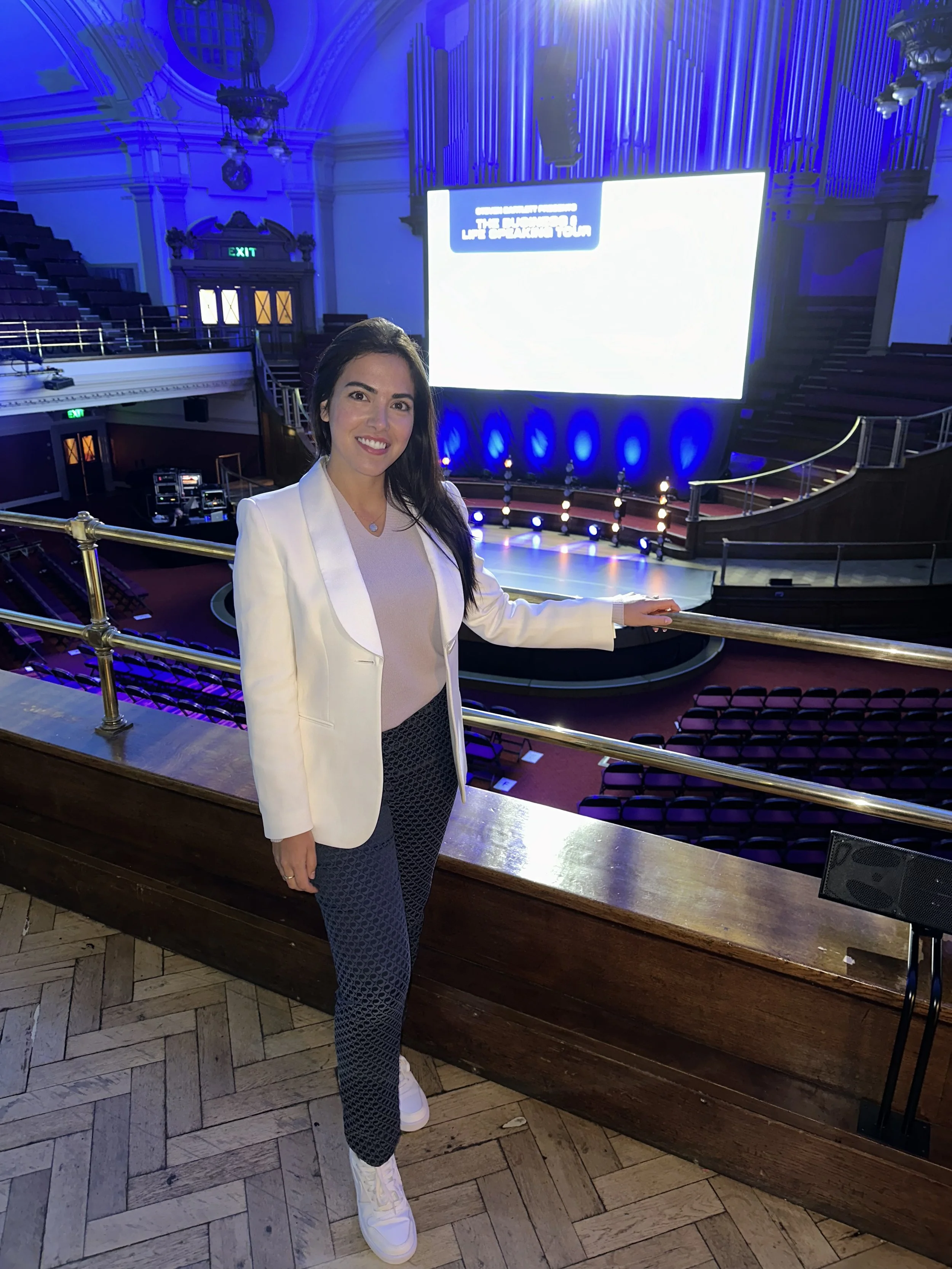 A person standing in an auditorium with a large screen and stage in the background, lit with blue lighting.