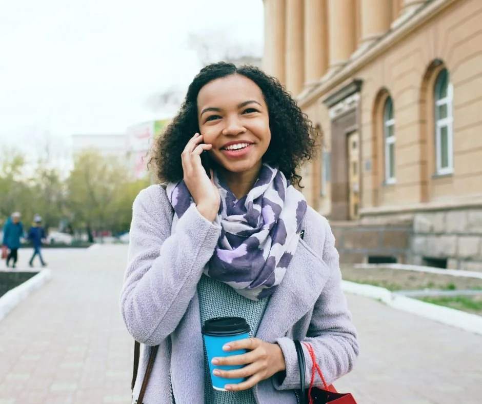 Smiling women talking on a cell phone outside, holding, a travel mug in the other ha